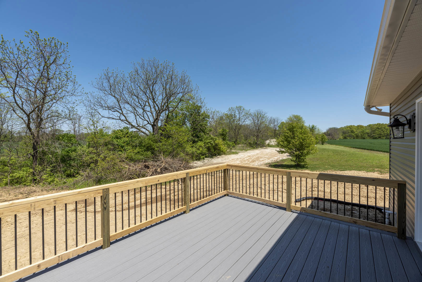Wooden deck with metal railing, bordered by a privacy fence, leafy green trees and bare branches in the background under a clear sky