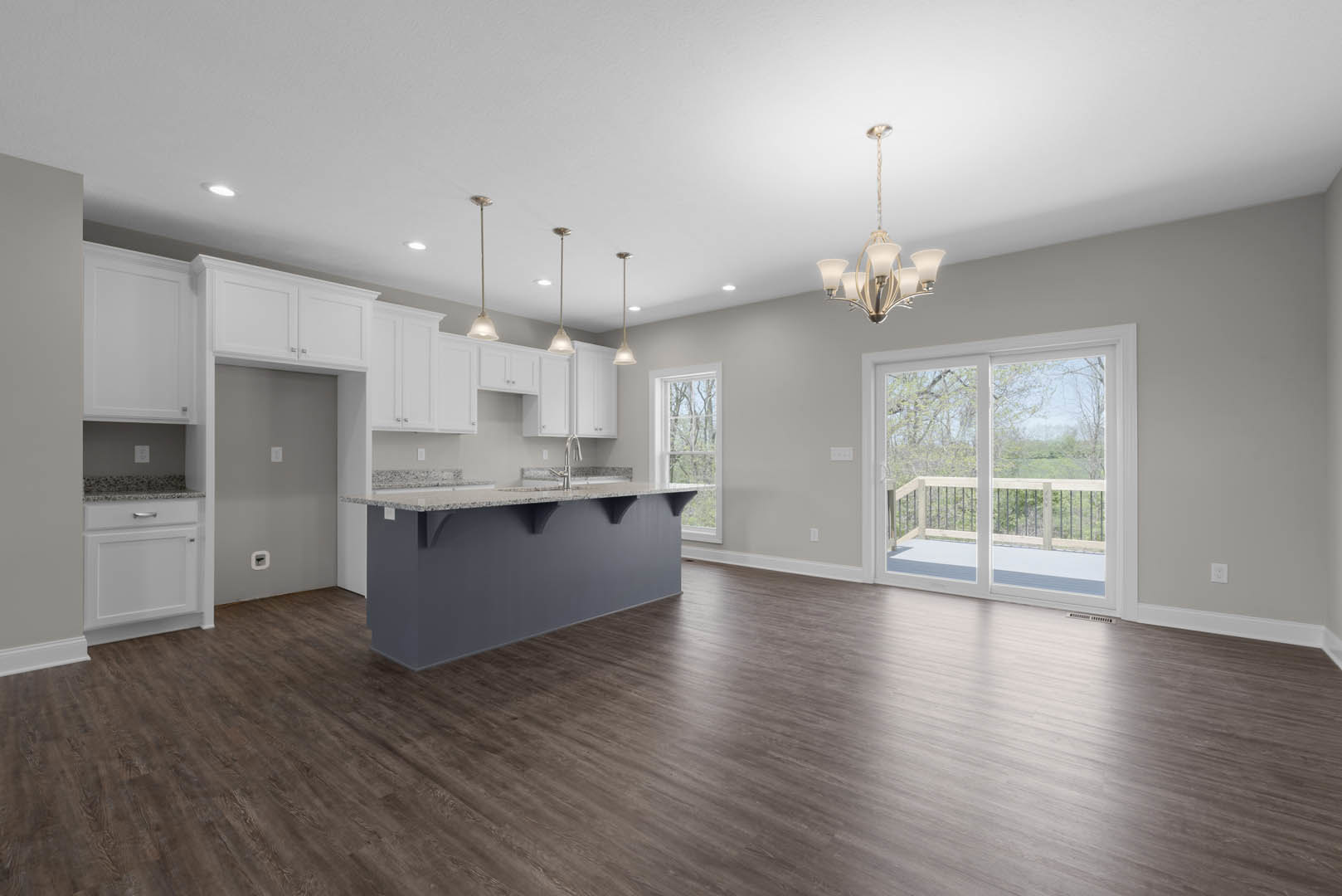 Open kitchen and dining area with wood flooring, grey accent wall, white-shaded chandelier, sliding glass door leading to balcony, and modern cabinetry.