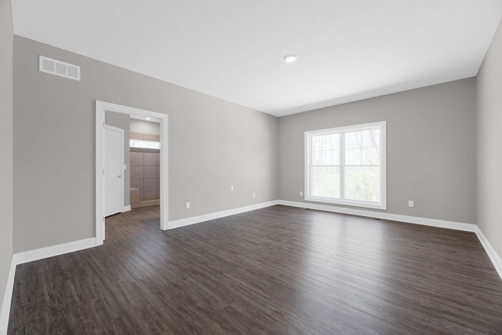 Room with light wood flooring, white paneled door, white-framed window, wall vent, and bathroom featuring white square tile wall
