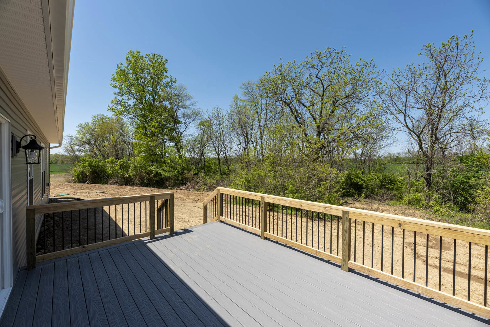 Wood deck with wooden railing, surrounded by leafy trees and a privacy fence in the background