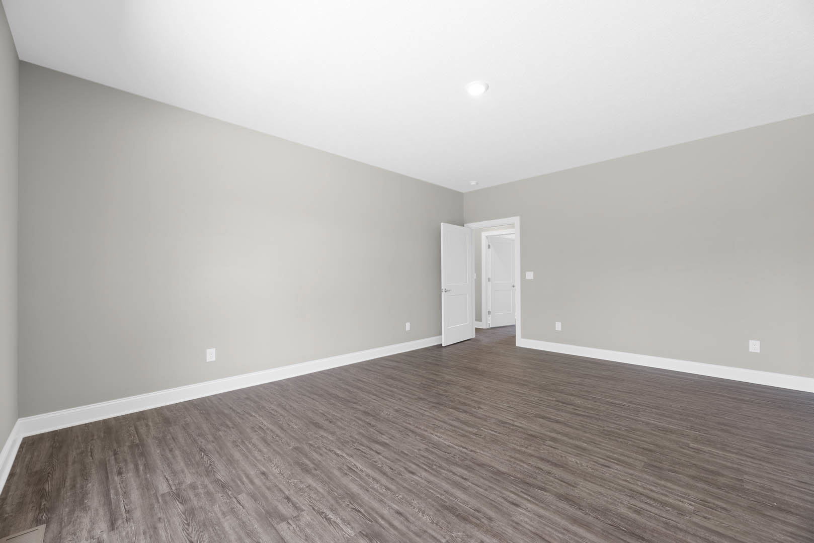Wood flooring in a room with white walls and a white door featuring silver handles and a mirrored panel