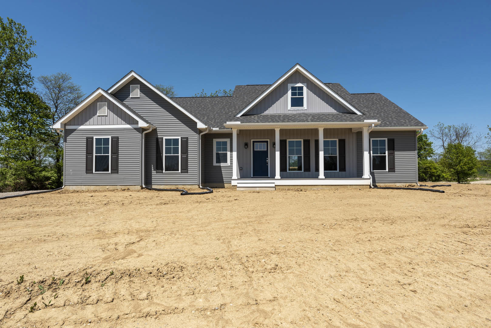Two-story house with blue and white doors, white-framed windows, and a dirt yard bordered by a tree with green leaves