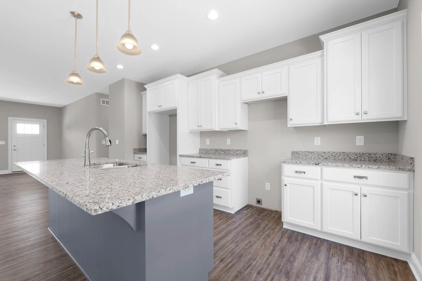 White kitchen with granite countertops, central island featuring a sink and silver faucet, white cabinets with silver handles, white door with window, light-colored walls and