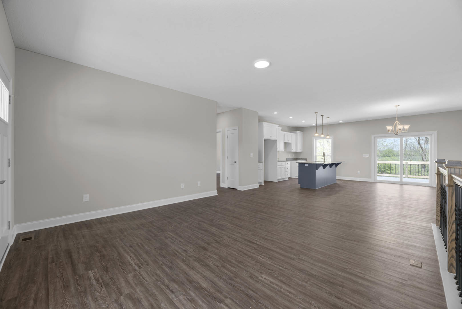 Spacious open-plan room featuring wood laminate flooring, white plaster walls, modern kitchen with glass countertop, dining area beneath a decorative chandelier, large window