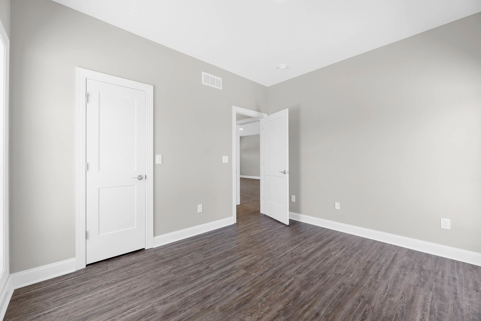 White paneled doors with silver handles, wood laminate flooring, white plaster walls, ceiling vent, and a close-up of the smooth white ceiling.