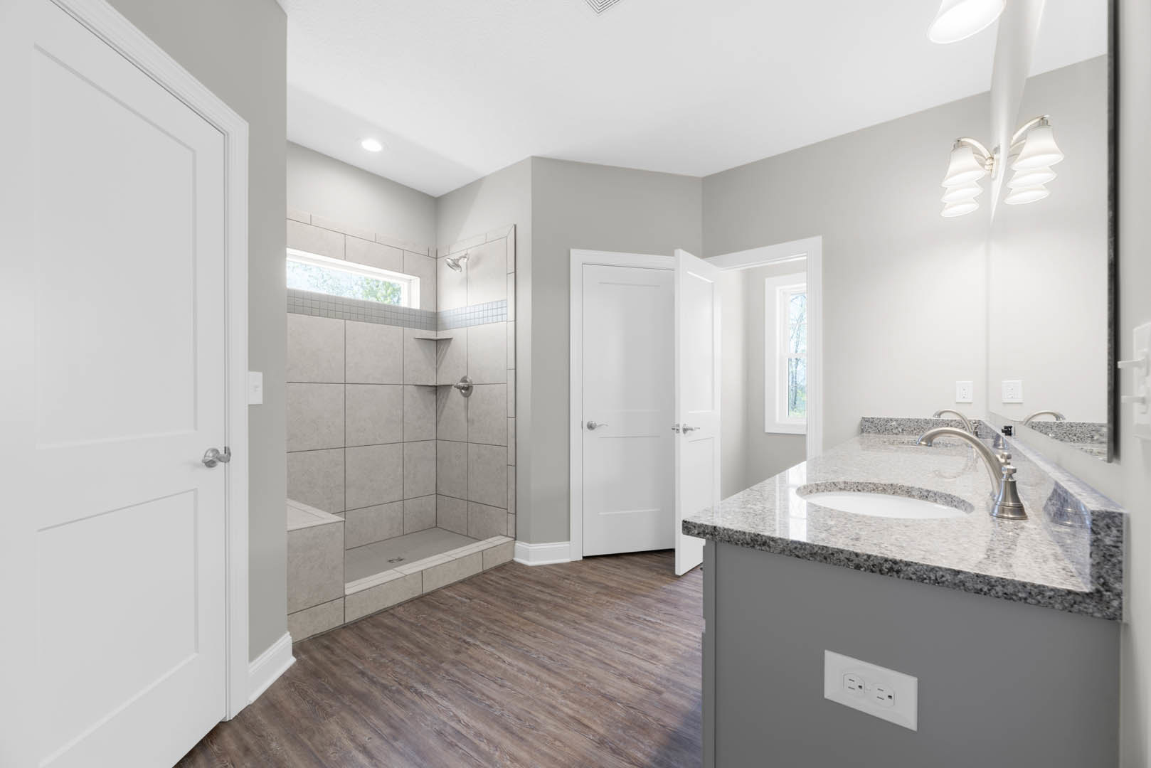 Bathroom featuring a glass-enclosed shower with a window, white vanity sink with chrome faucets, wood flooring, built-in shelving, and a white door with a silver handle
