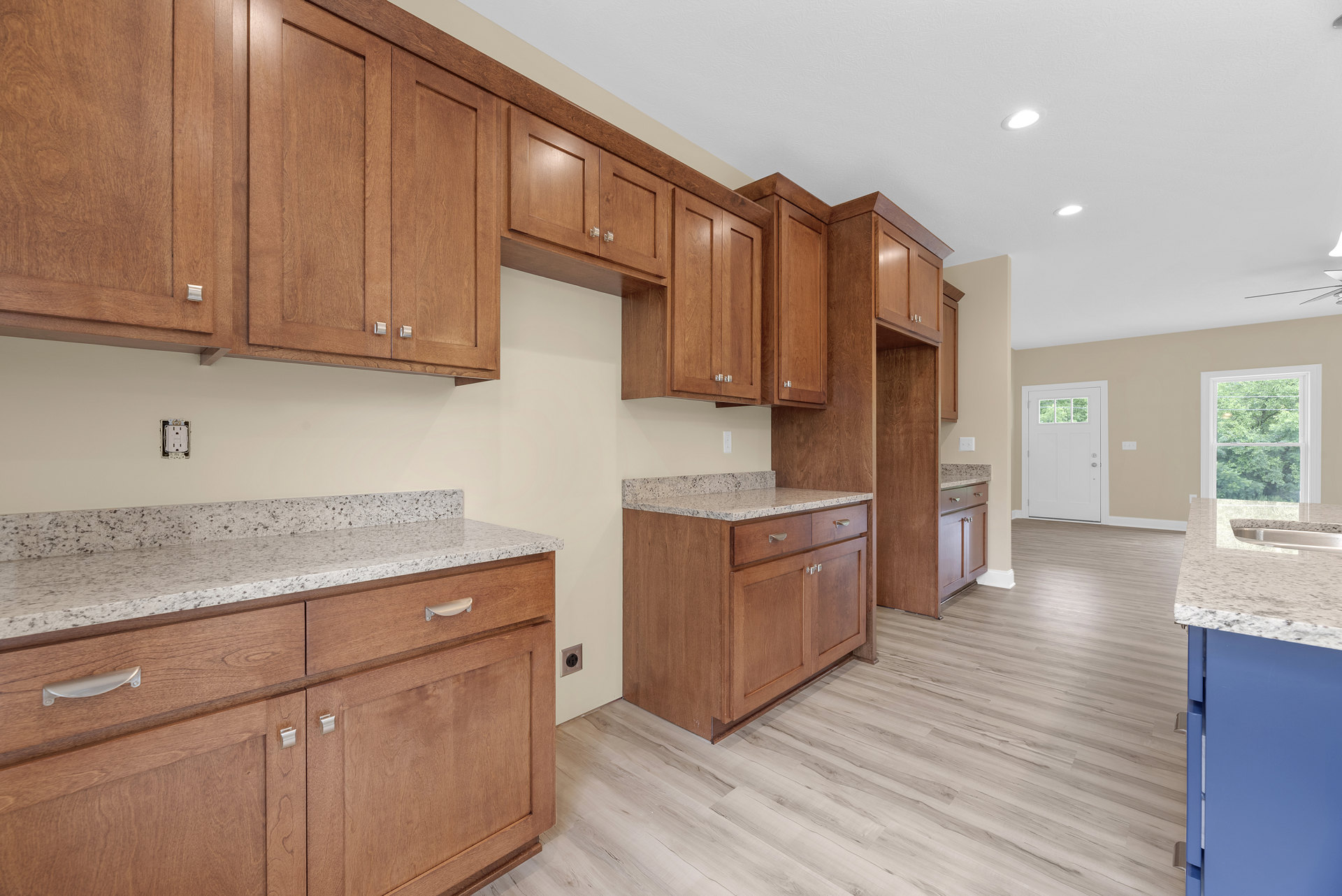 Kitchen featuring wooden cabinets, marble countertops, stainless steel sink, white door with window, large window overlooking trees, and light wood flooring