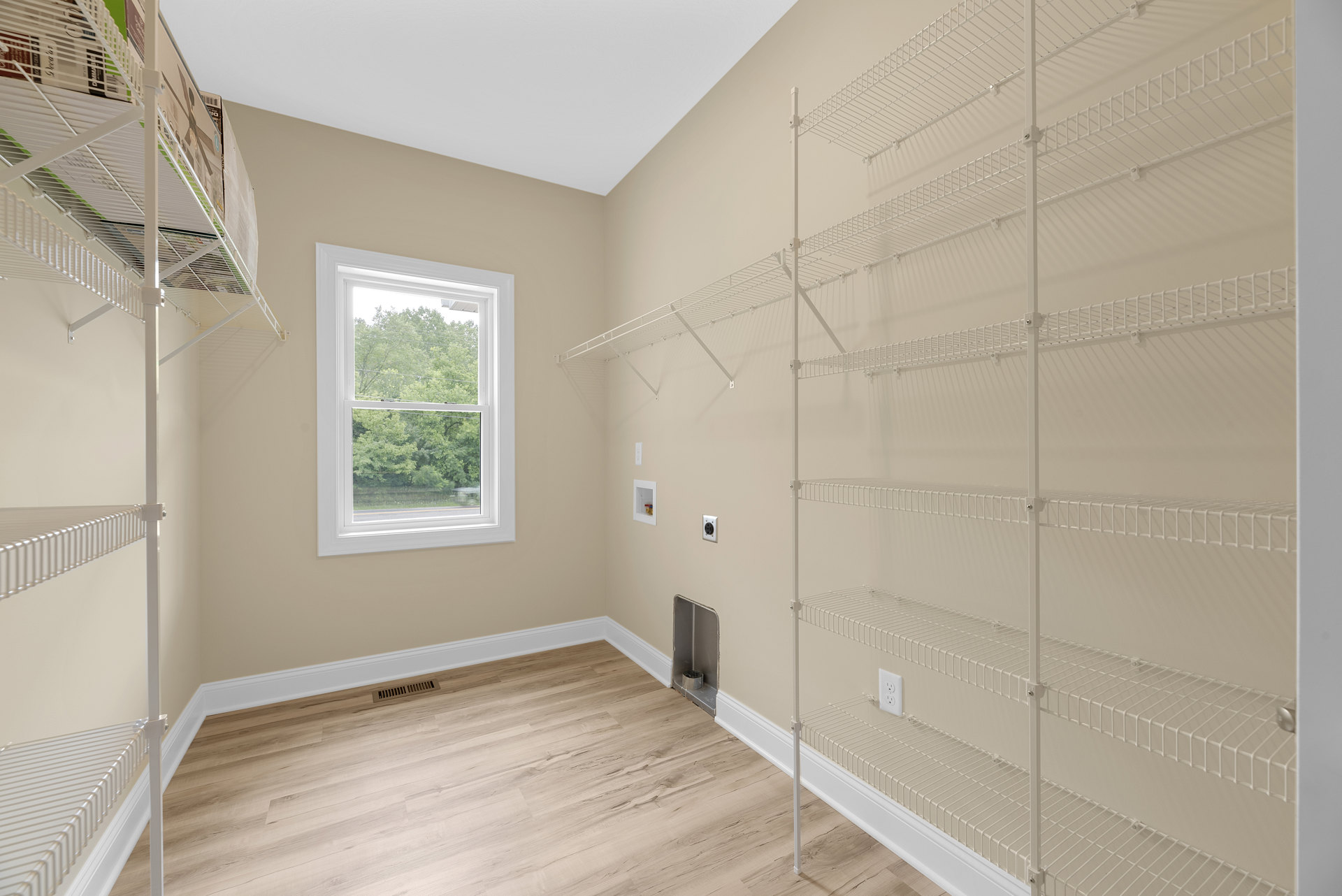 Wood-floored room with built-in shelves, boxes, metal container in corner, large window overlooking trees
