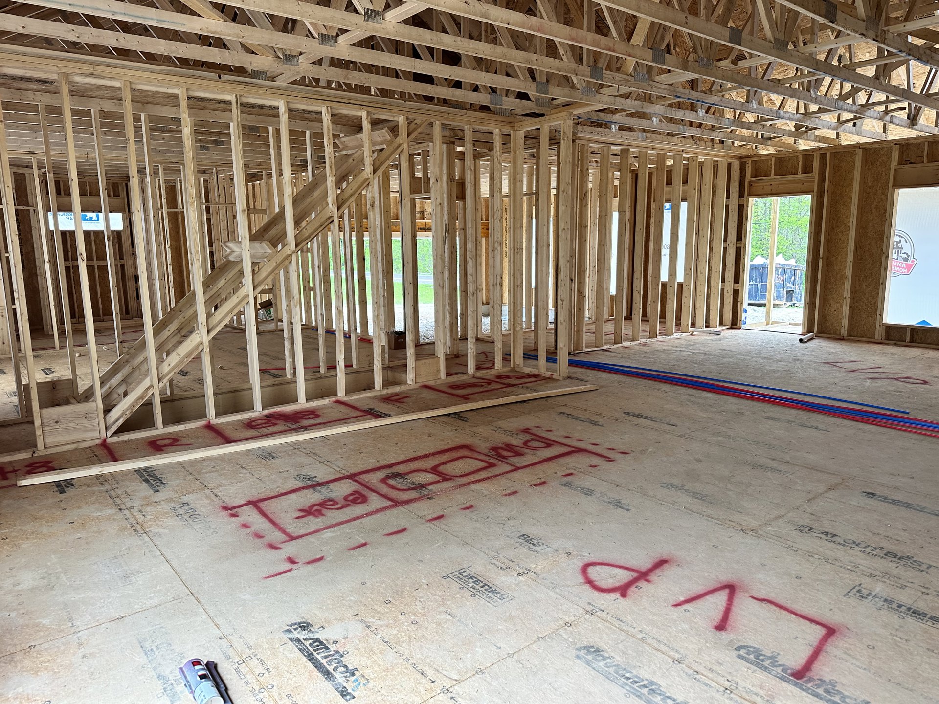 Exposed wooden beams and framing inside a house under construction, unfinished floor marked with red lines, blue container with white paint nearby