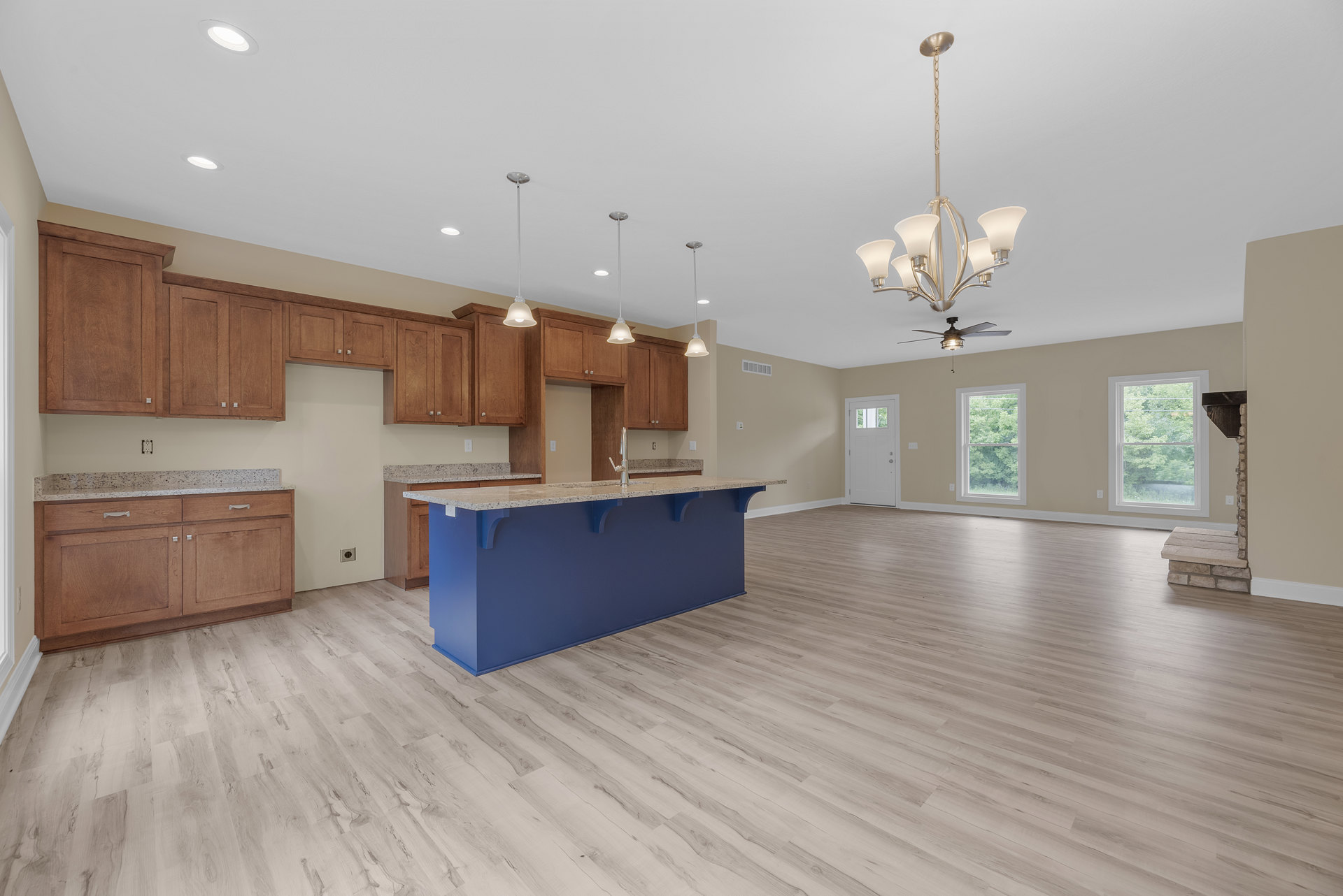 Blue kitchen island with silver faucet, marble countertop, wood flooring, white cabinetry, large window showing trees, white door with glass panel.