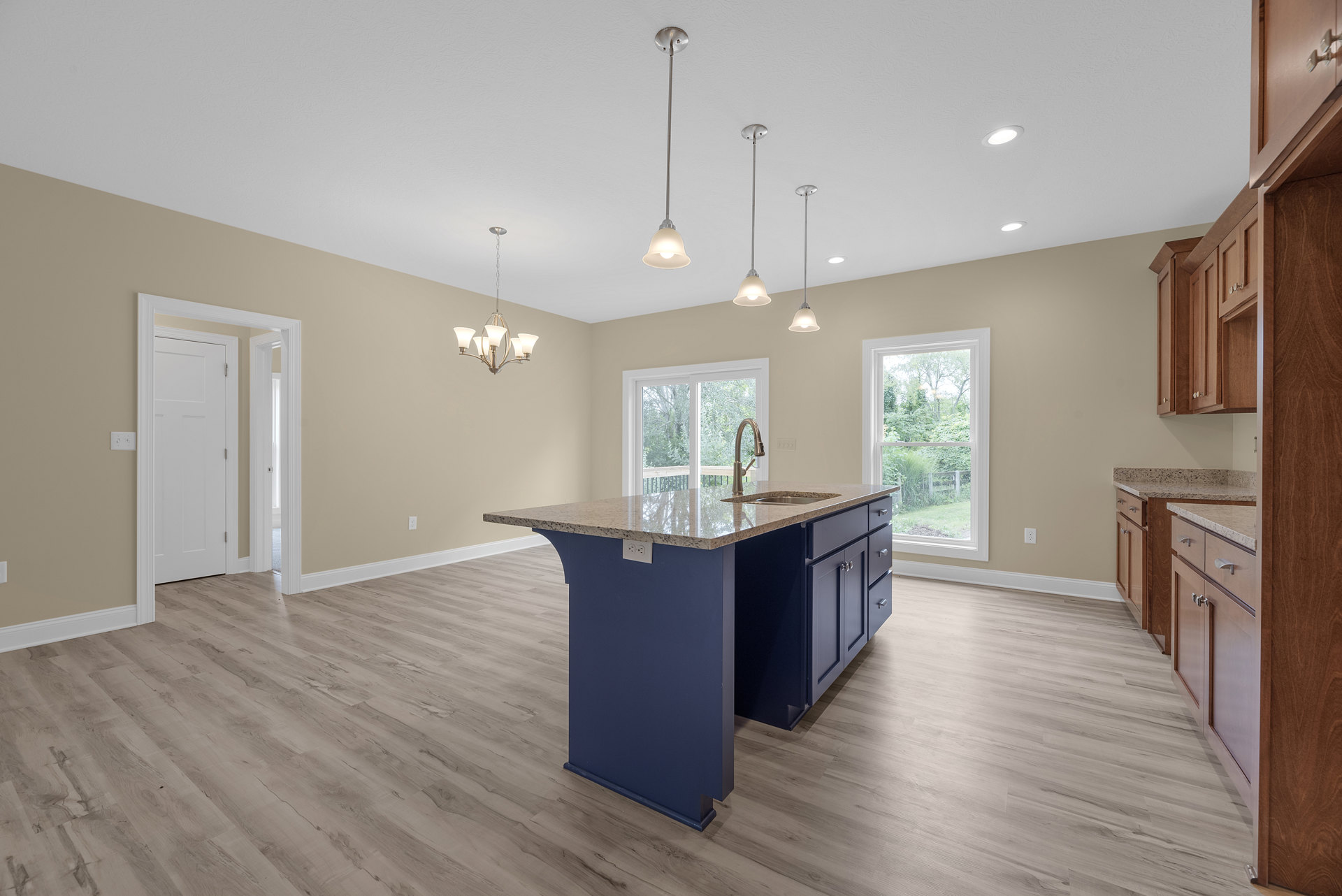 Kitchen with wood flooring, central island featuring built-in sink, white cabinetry, stainless steel fixtures, large window overlooking trees, white door with silver knob, modern