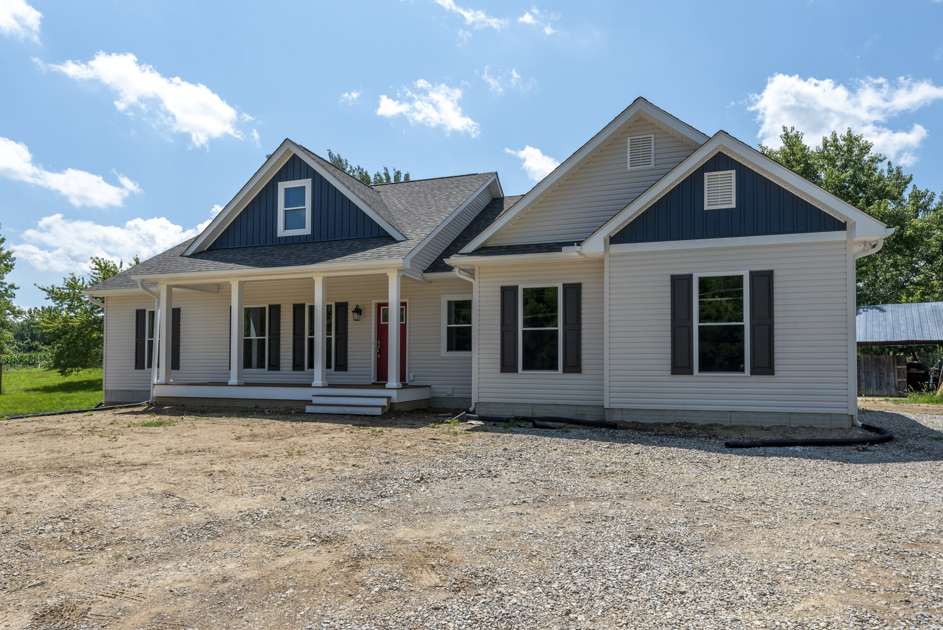 Gravel driveway leading to a blue-sided house with white trim and red front door, porch, and windows; Robert Frost Farm visible in the background under a clear blue sky.