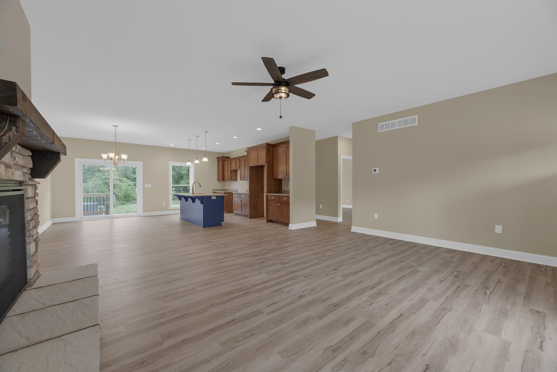 Spacious open floor plan featuring hardwood flooring, ceiling fan with light, blue kitchen island topped with marble, television, blue and white column, chandelier, and large