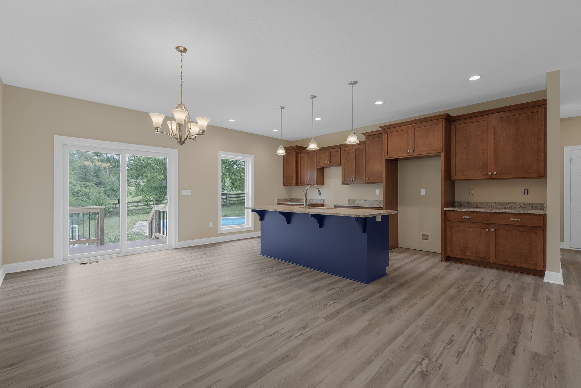 Blue kitchen island with built-in faucet, wood flooring, sliding glass door opening to backyard, chandelier hanging from ceiling, wooden railing with black metal bars, blue accent