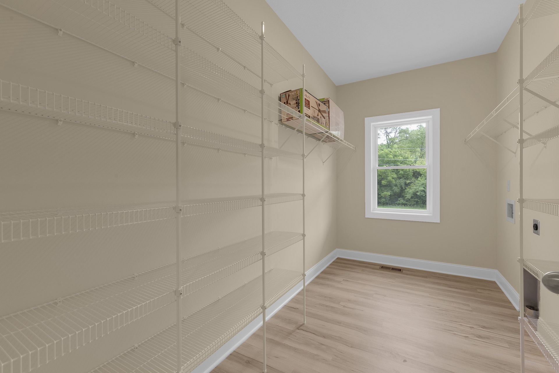 White built-in shelves with storage boxes and a metal rod, wood flooring, large window with trees visible outside, plaster walls and ceiling molding