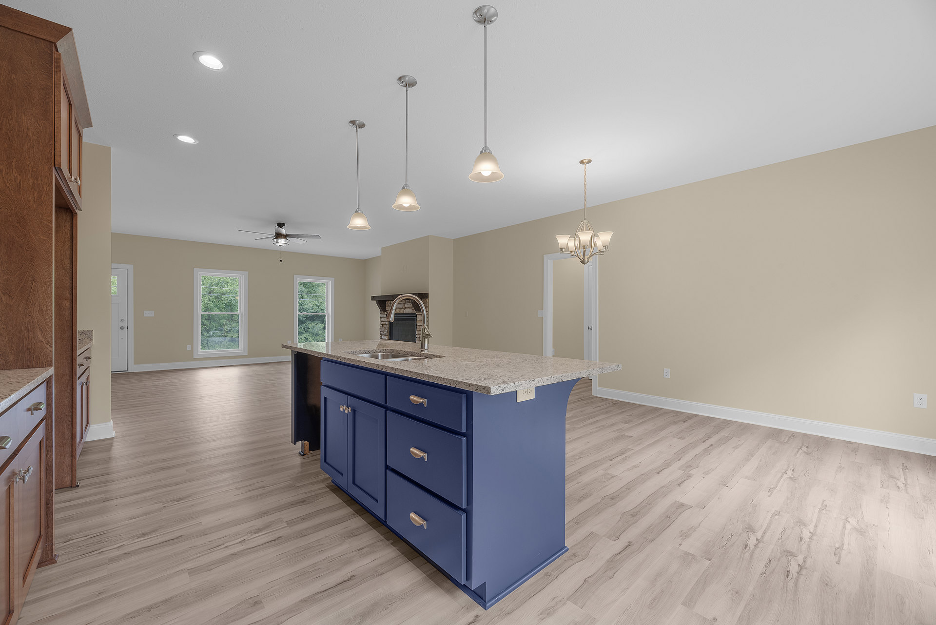 Blue kitchen island with built-in sink, white cabinetry, wood flooring, ceiling fan with light, large window revealing trees outside, white walls, and slim metal support pole