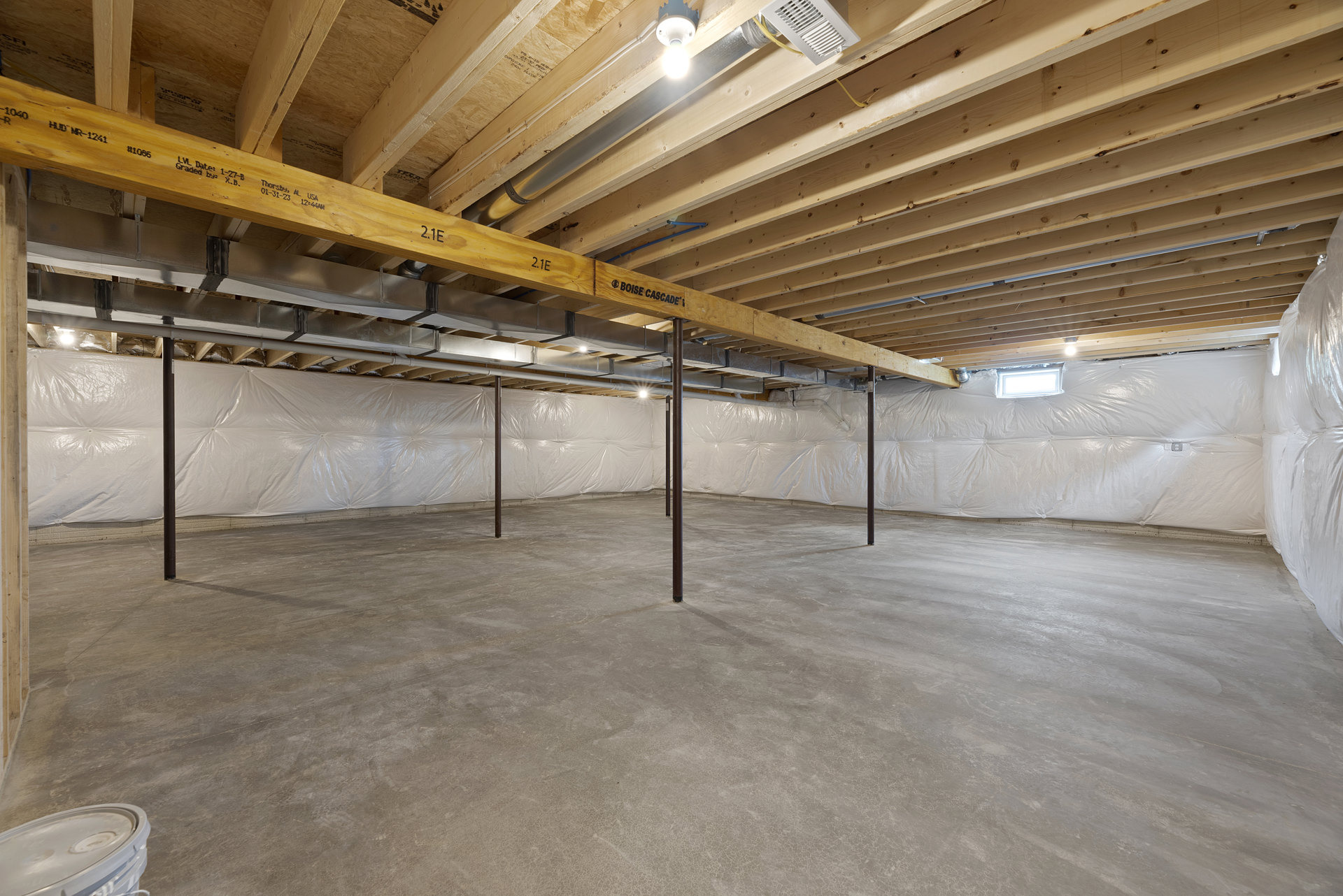 Concrete floor with exposed metal support poles, unfinished wooden ceiling, white insulation sheet partially covering beams, single light bulb hanging from ceiling