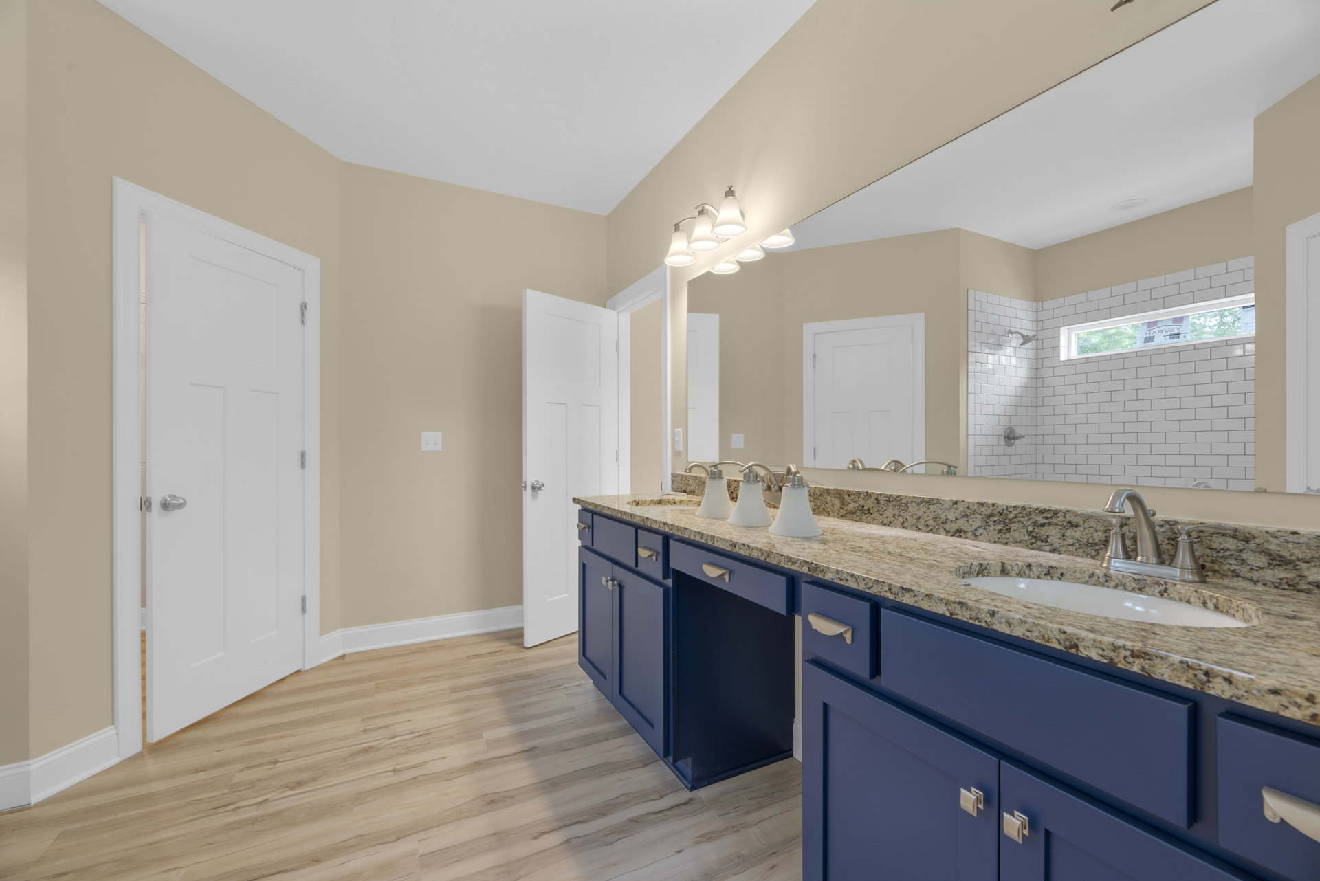Bathroom with blue cabinets, marble countertops, large wall mirror, white door with silver knob, and close-up of sink and soap dispenser