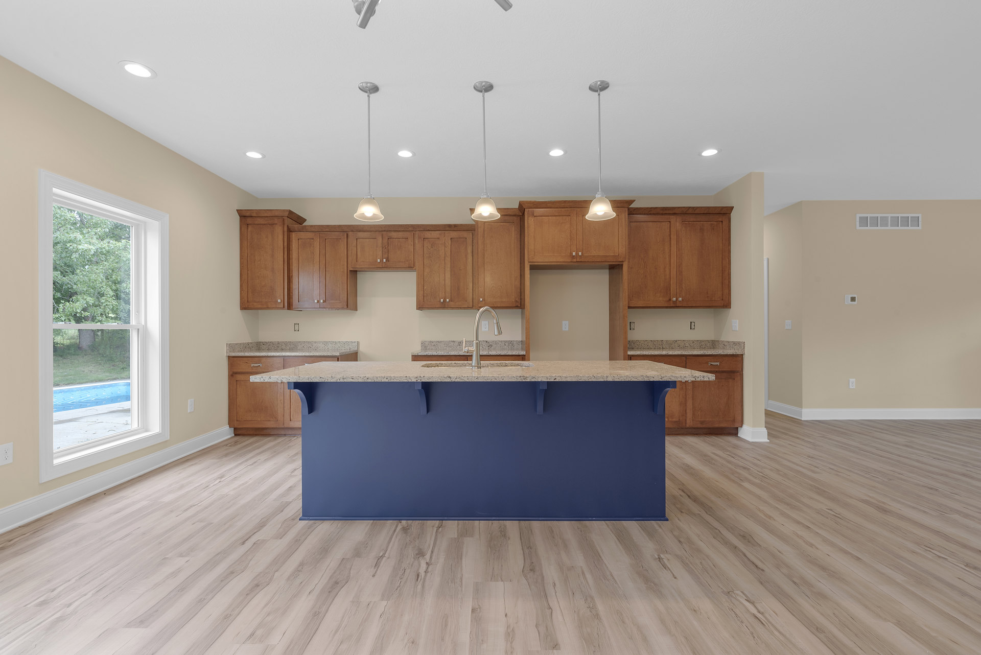 Blue kitchen island with white countertop, stainless steel sink and faucet, wood flooring, white cabinetry, large window overlooking trees, light blue accent wall