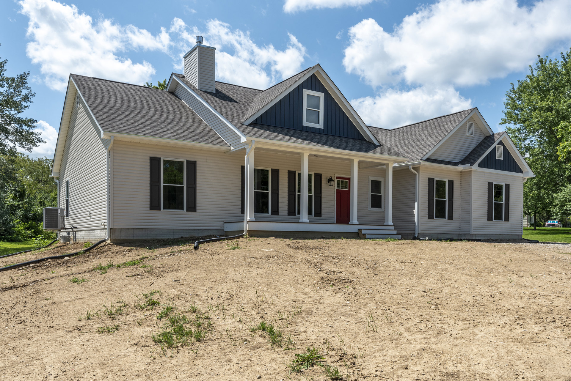 Two-story house with white siding, red front door, and white-framed windows, set beside a dirt hill with patches of grass; Robert Frost Farm visible in the background under a