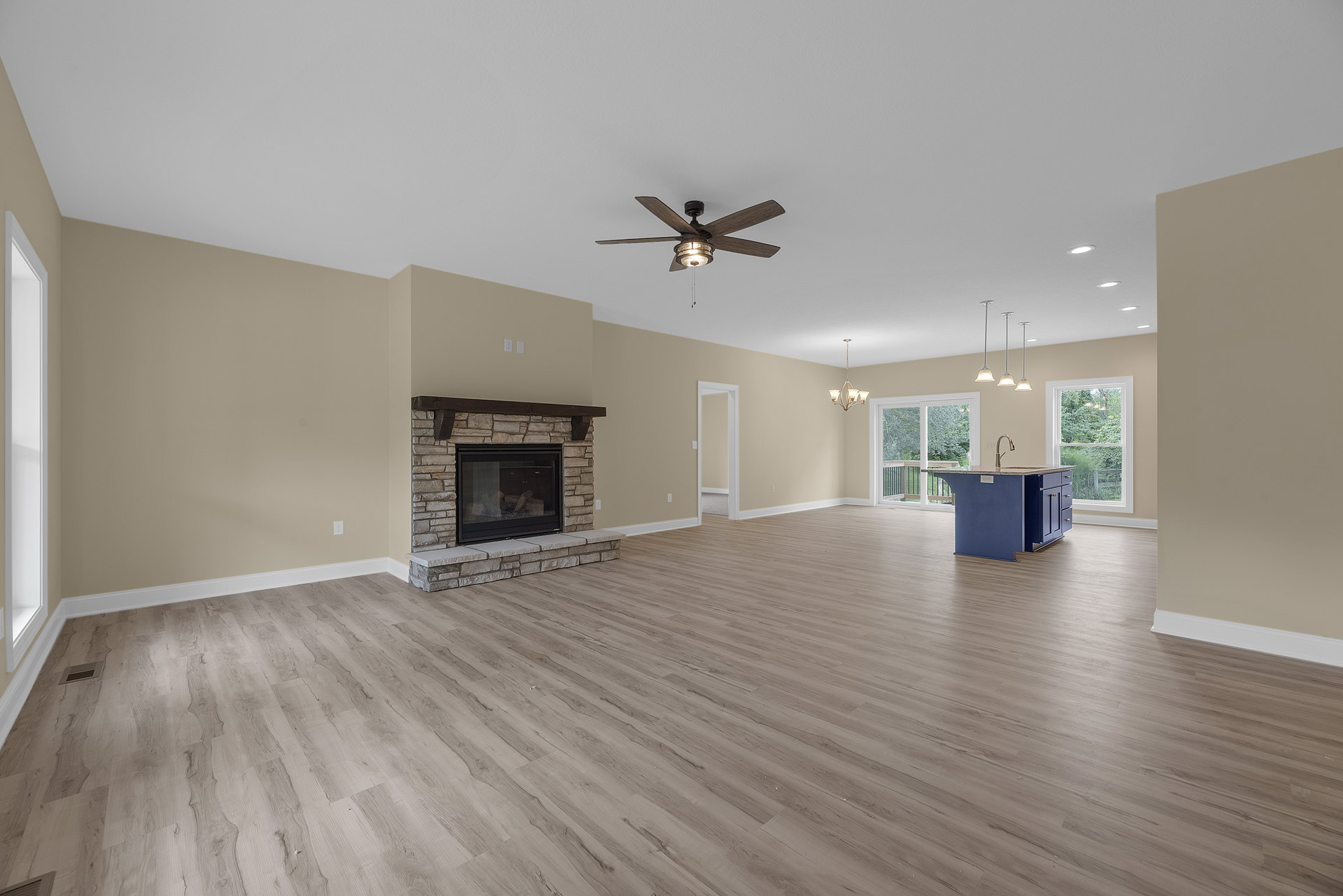Spacious living room featuring hardwood floors, a fireplace with a wood mantle and glass door, ceiling fan with light, and a blue kitchen island topped with marble