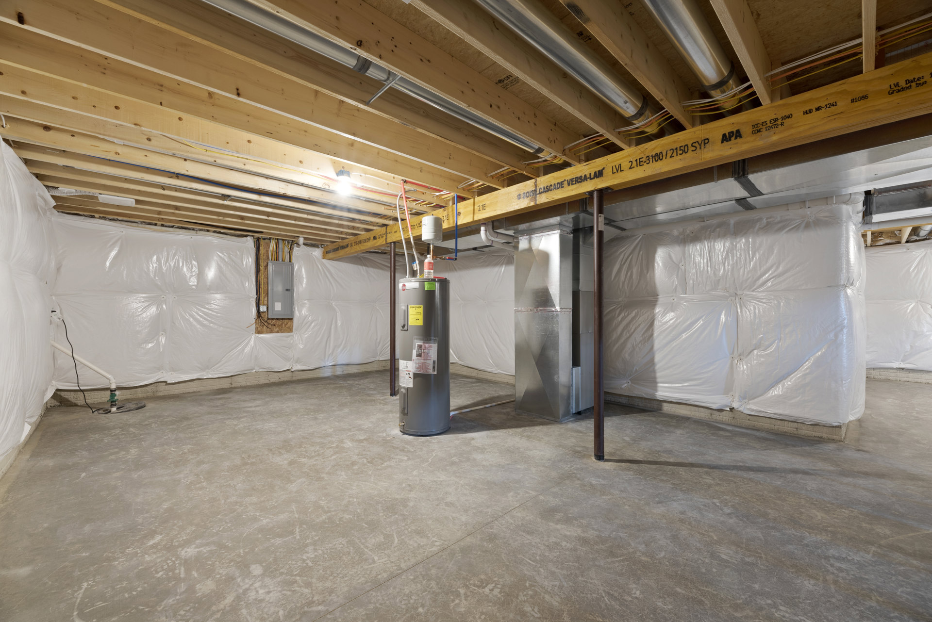 Unfinished utility room with exposed wood beams, concrete floor, large cylindrical water heater with white label, and rectangular metal container secured with tape.