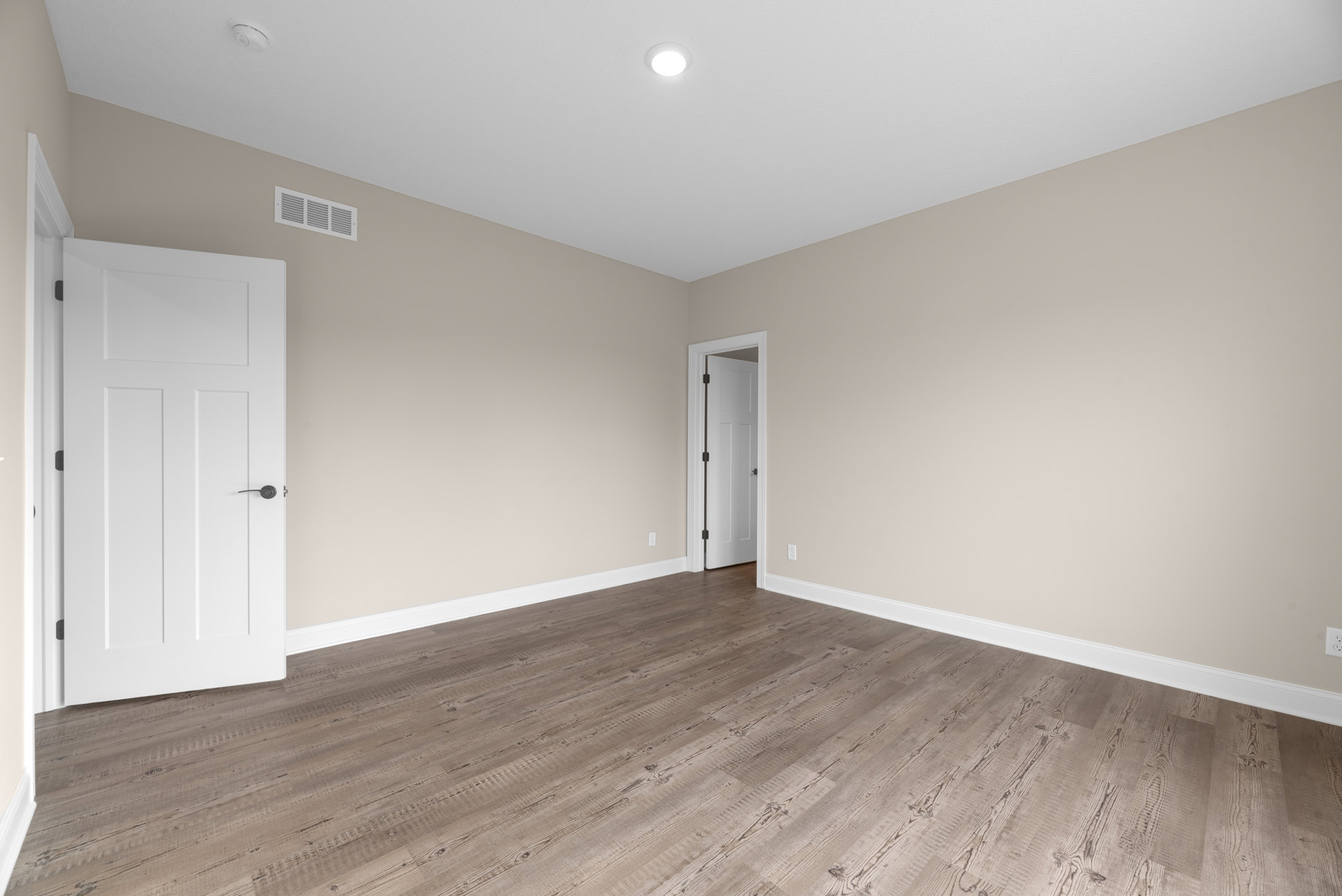 White door with black handle and ceiling vent, wood laminate flooring with white baseboard trim, recessed ceiling light, smooth plaster walls
