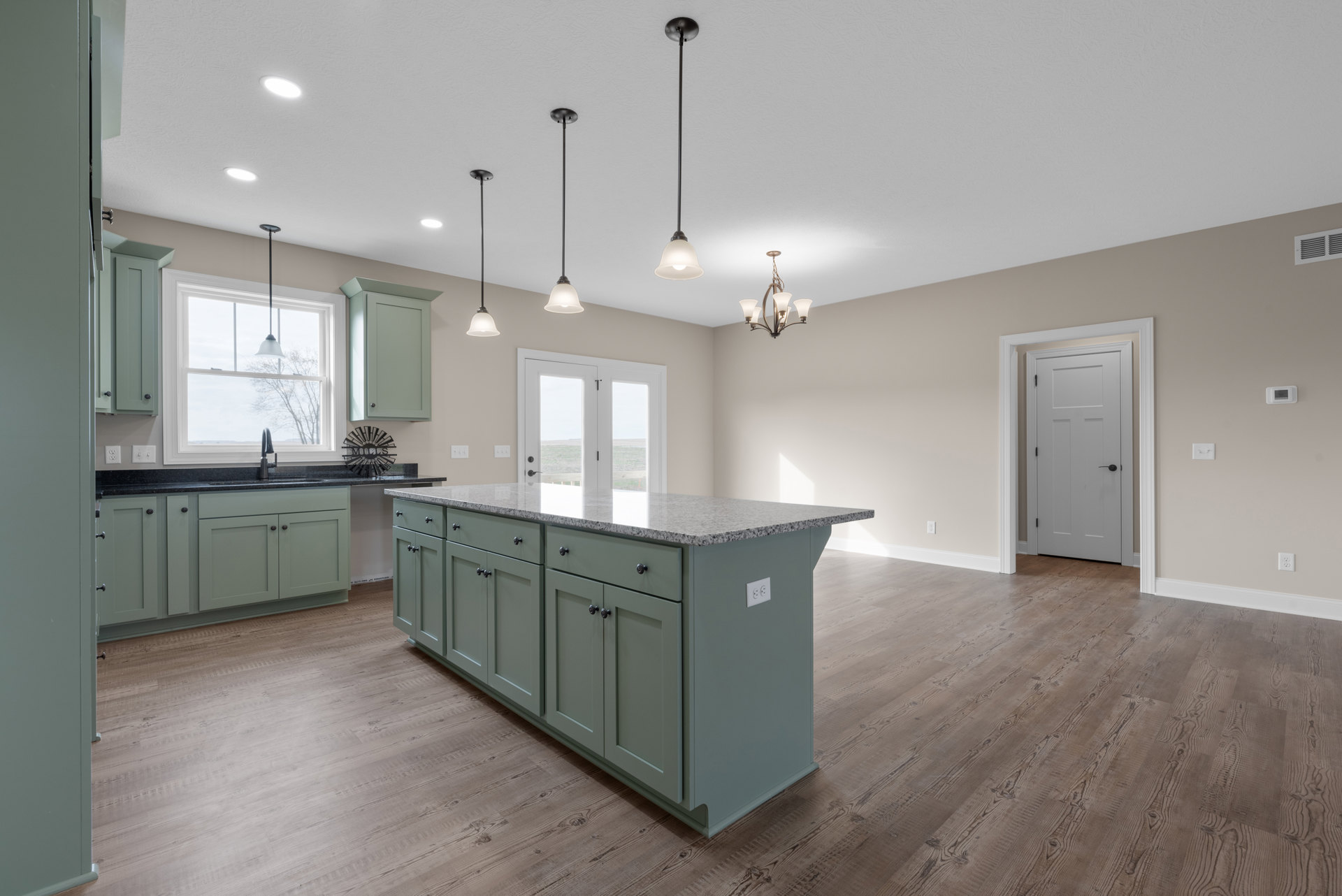 Kitchen with wood flooring, central island featuring granite countertops, white cabinetry, stainless steel sink, white door with black handle, black metal sunburst sign mounted on