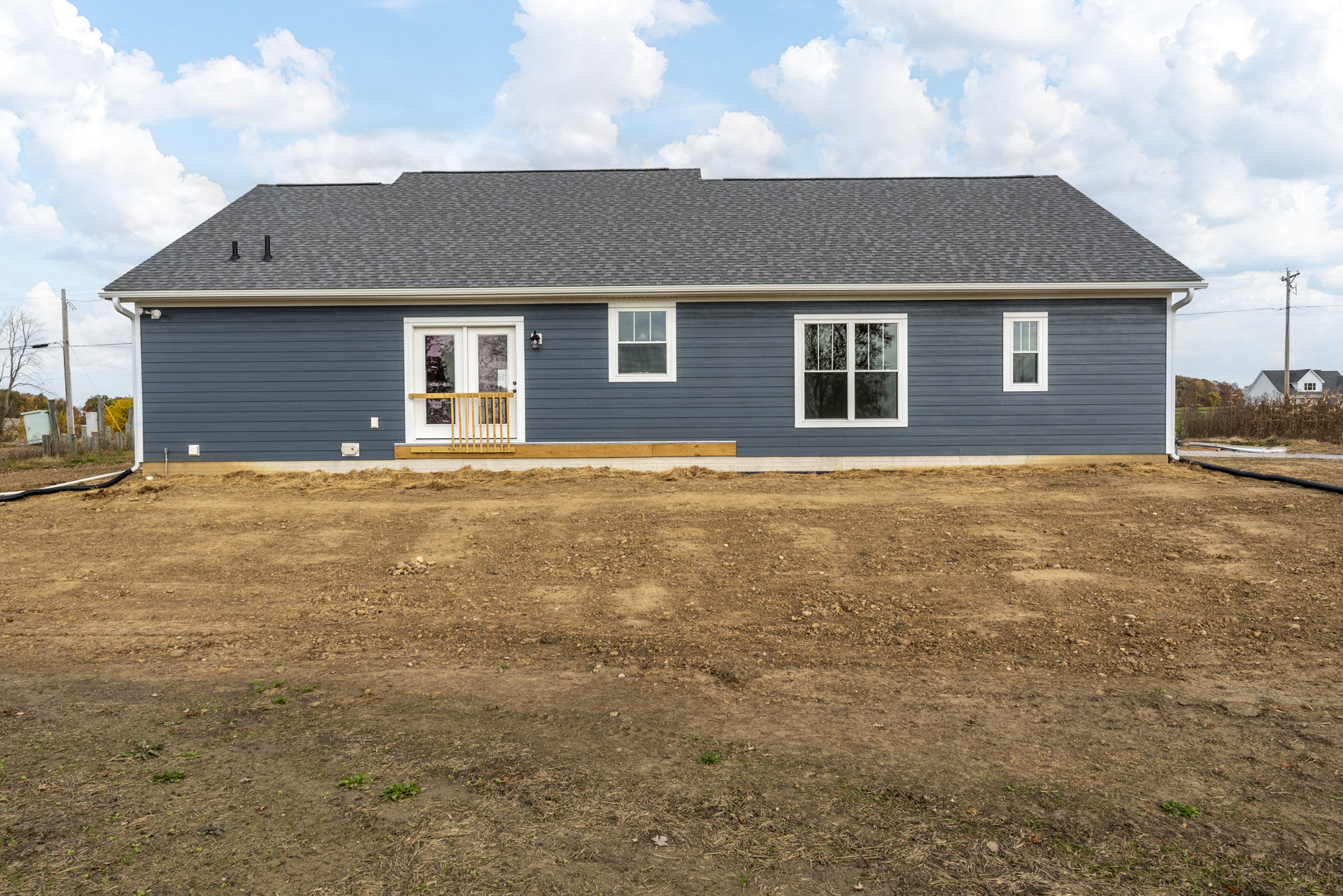 Two-story house with blue siding, white trim windows, covered porch, white front door, wooden railing, and dirt yard under a cloudy sky