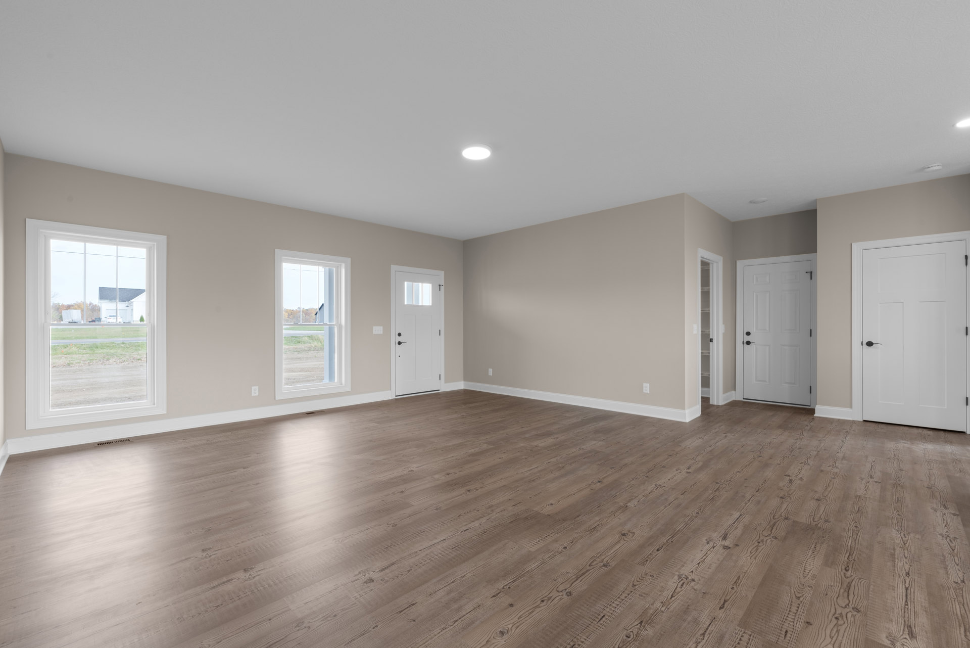 White paneled doors with black handles, wood plank flooring, white walls, and a window overlooking a road and neighboring house