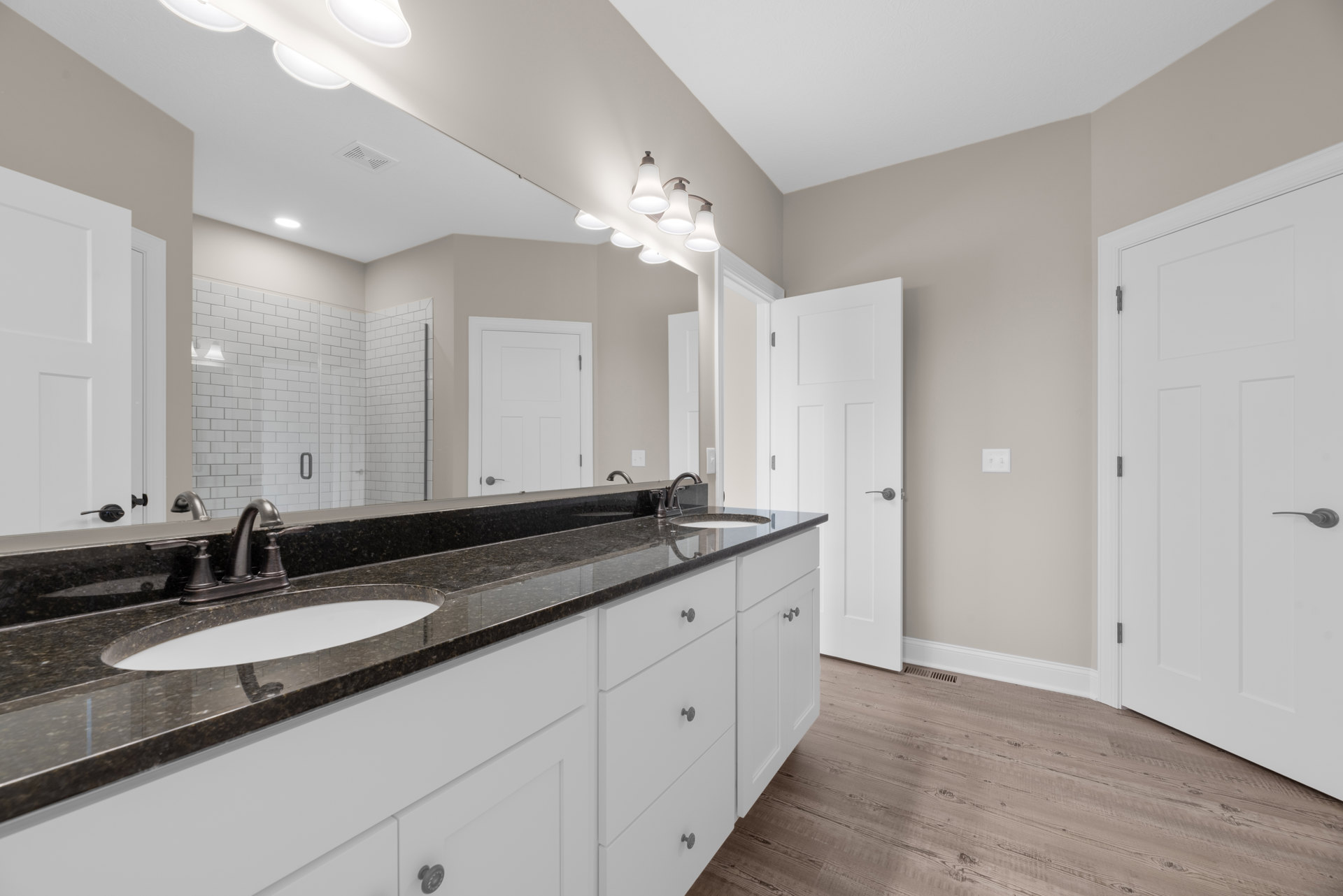 Bathroom featuring a wide framed mirror above a double sink vanity with stone countertop, modern faucets, glass-enclosed shower, freestanding bathtub, white door with matte black