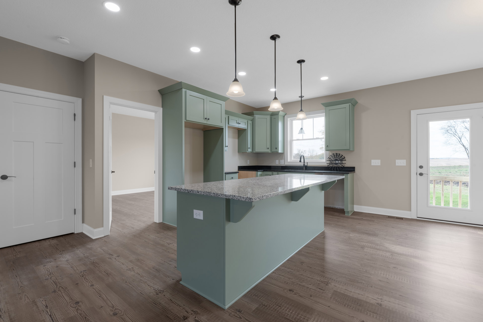 Kitchen with wood flooring, central island featuring granite countertops, white cabinetry, stainless steel sink, metal wall sign, white door with black handle, door offering view