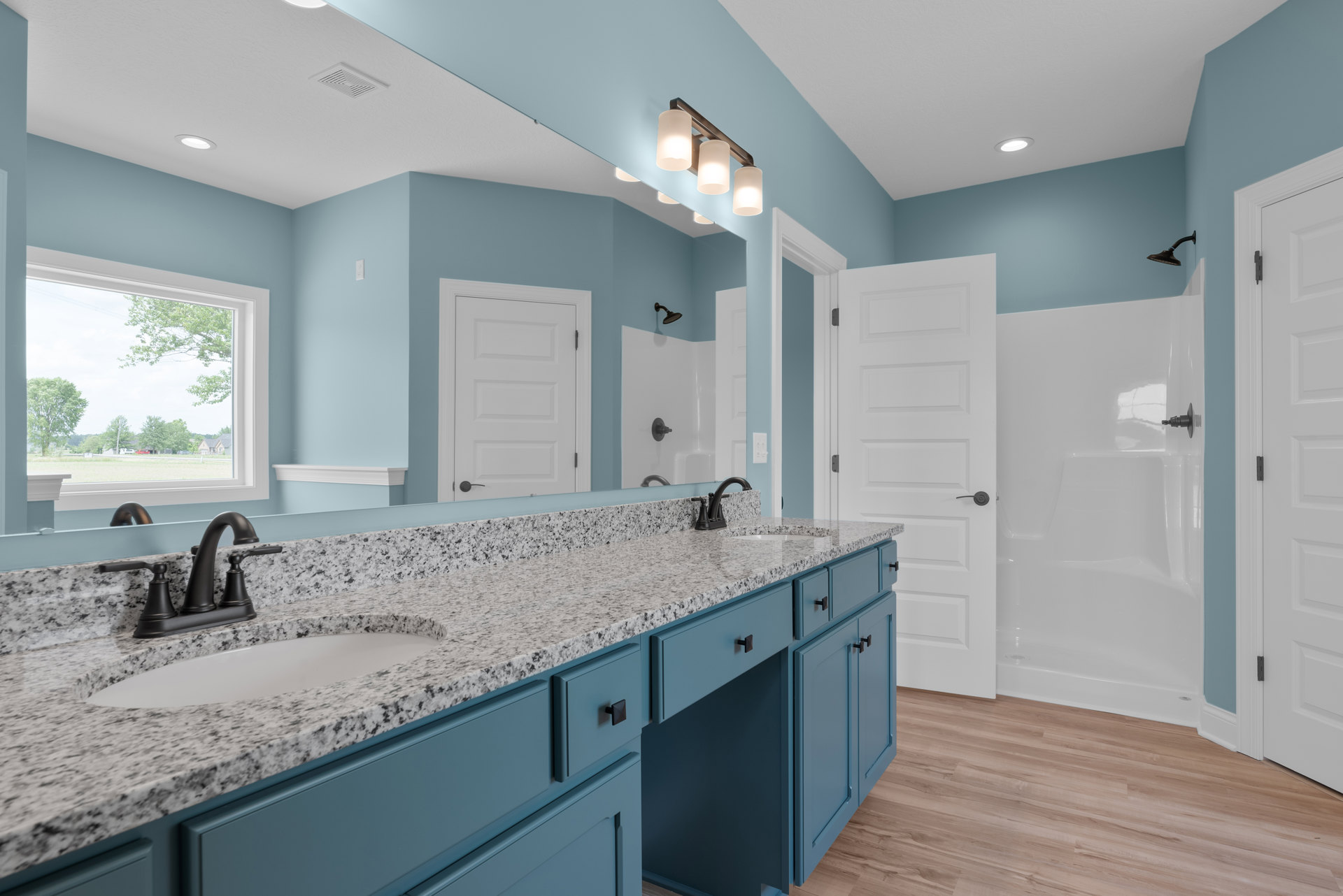 Bathroom with blue painted walls, marble countertop, blue cabinetry, black faucet, black shower head, white door with black hinges, and modern light fixture above sink.