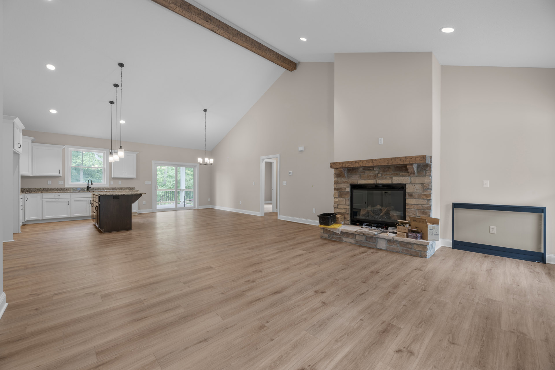 Spacious living room featuring hardwood floors, central stone fireplace, white wall outlet, sliding glass door opening to balcony, and open floor plan with neutral walls and