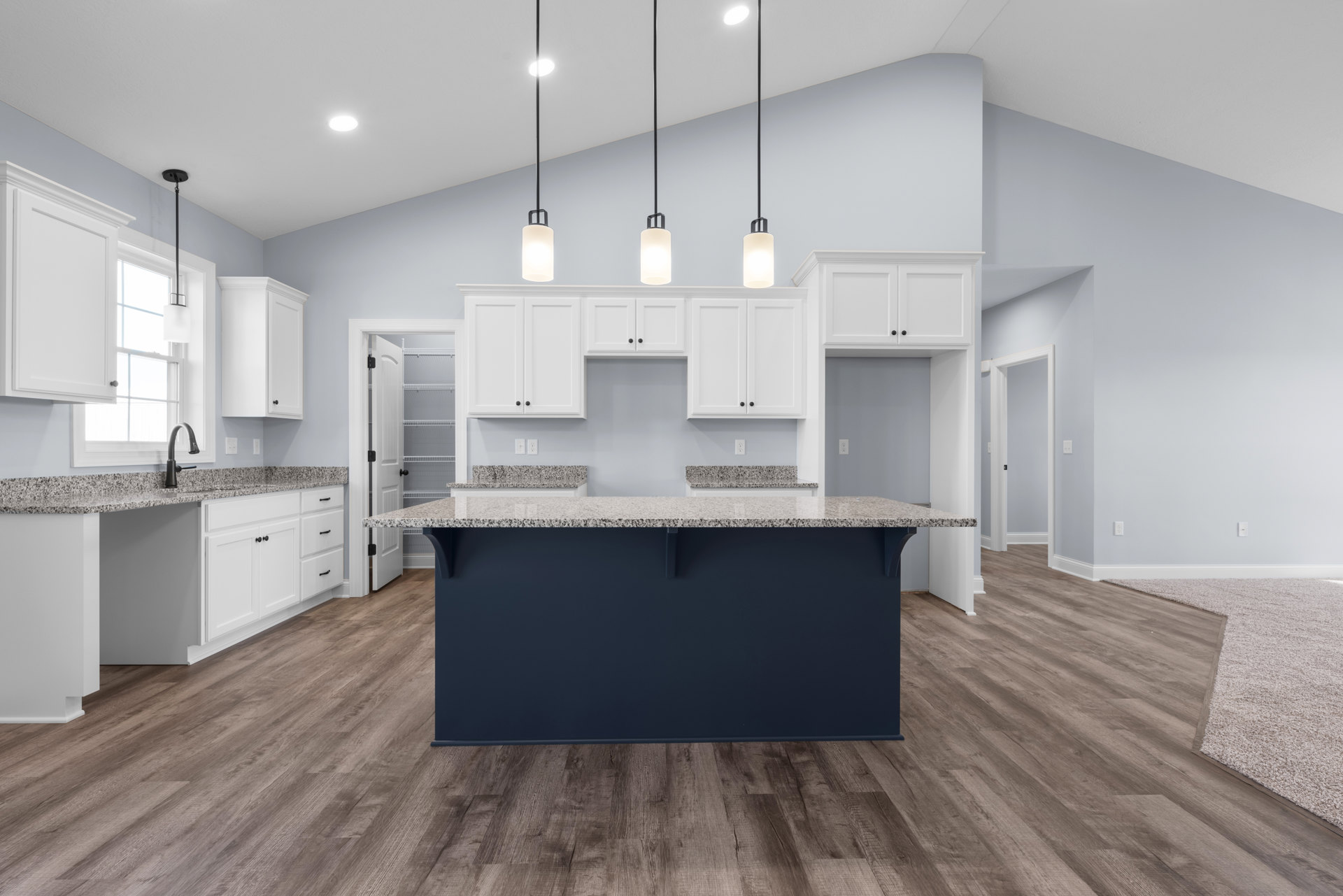 Kitchen with white shaker cabinets, dark blue accent wall, wood flooring, white door with black handle, and light-colored countertop with integrated sink.