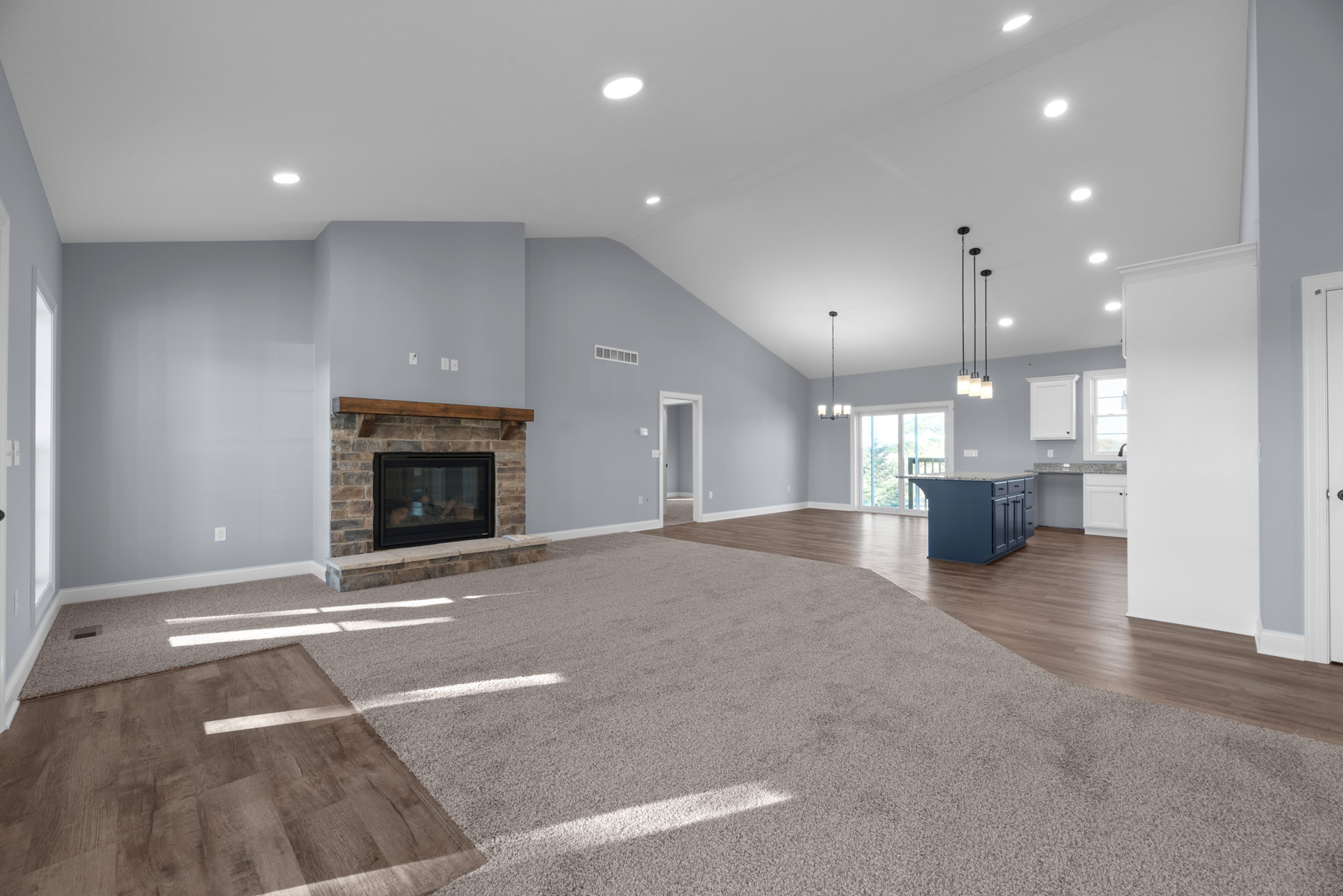 Spacious living room featuring a marble-topped kitchen island, glass fireplace door, white door with black knob, light wood flooring, and carpeted area adjacent to kitchen with