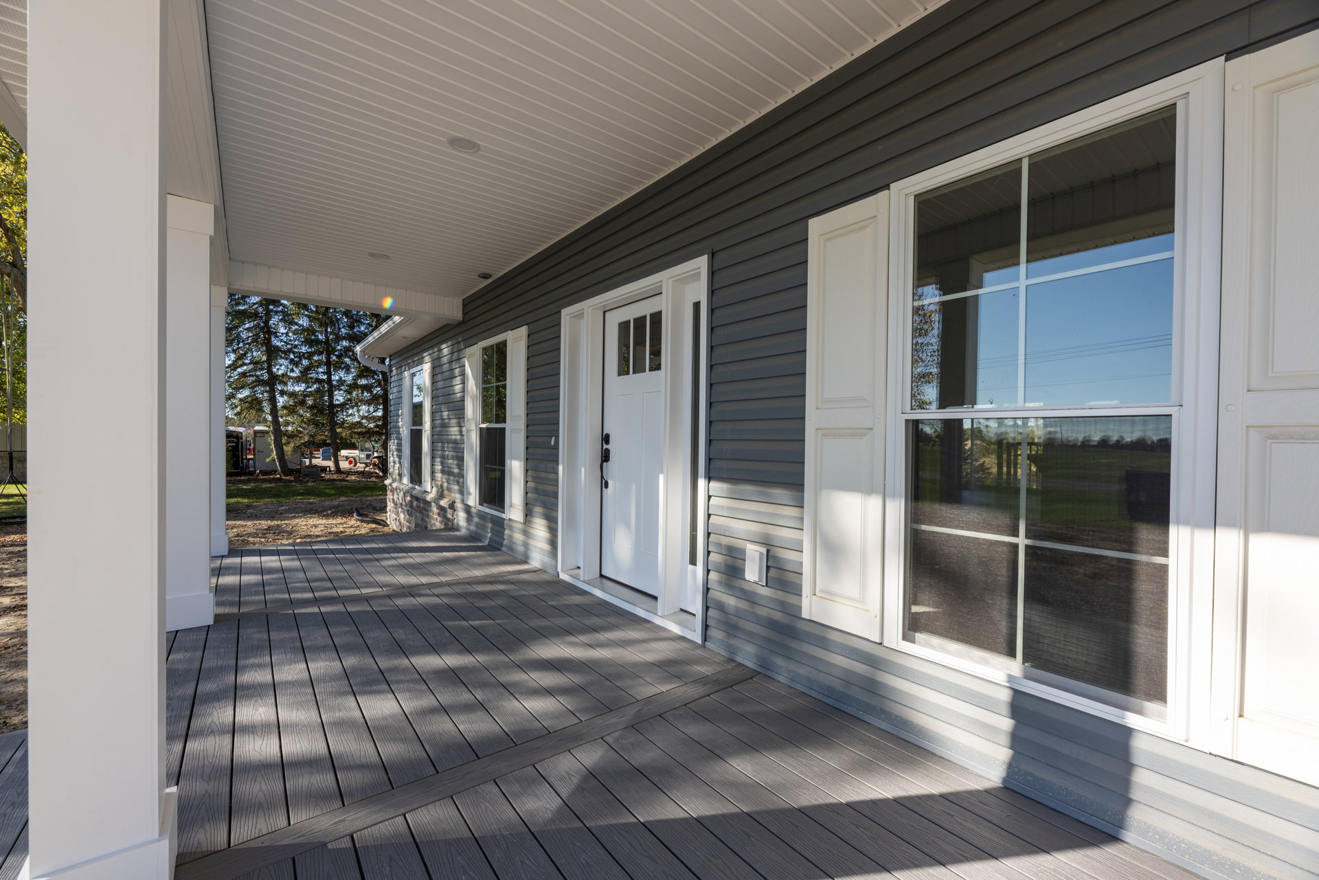 Wood deck with cross-braced railing, white doors and windows, screened window, porch area, surrounded by trees and composite siding