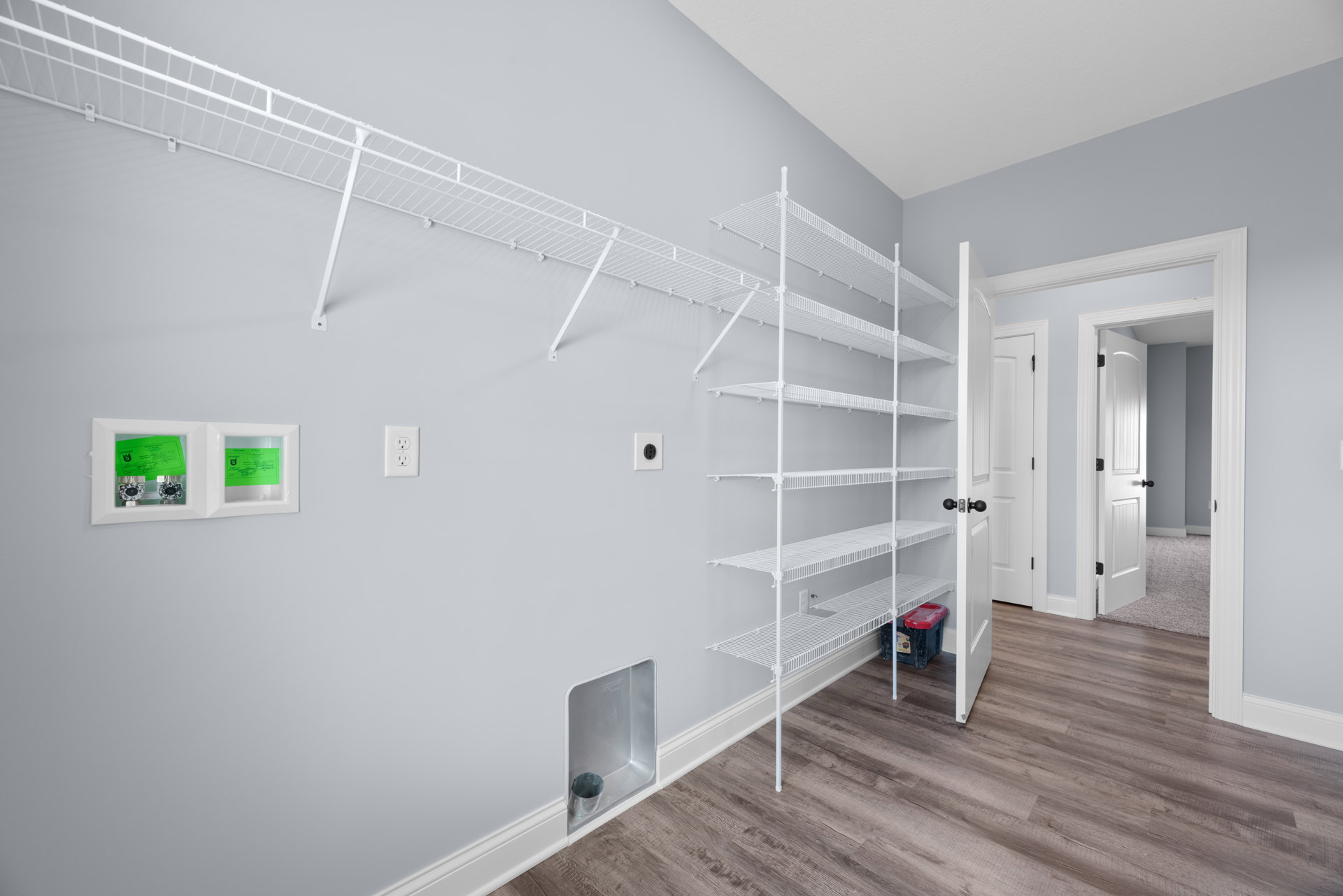 Built-in white shelving unit against plaster wall, light wood flooring, assorted storage boxes, washing machine partially visible in foreground.