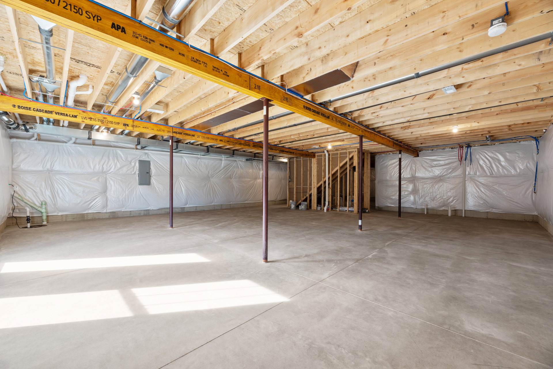 Exposed wooden ceiling beams, white pipe with green tape, concrete floor with support pole, unfinished walls, smoke detector mounted on wood surface
