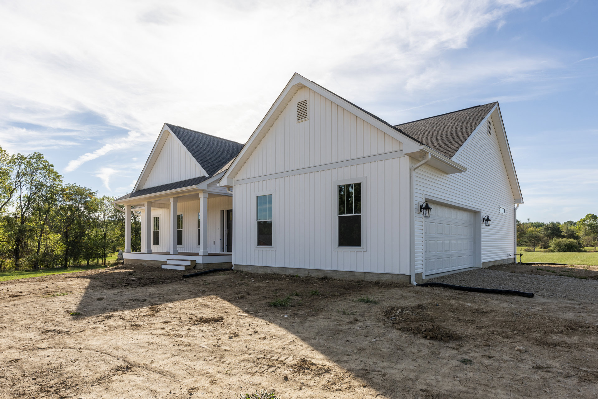 White siding house with covered porch, white-framed windows, paved driveway, and Robert Frost Farm visible behind a cluster of trees under a partly cloudy sky.