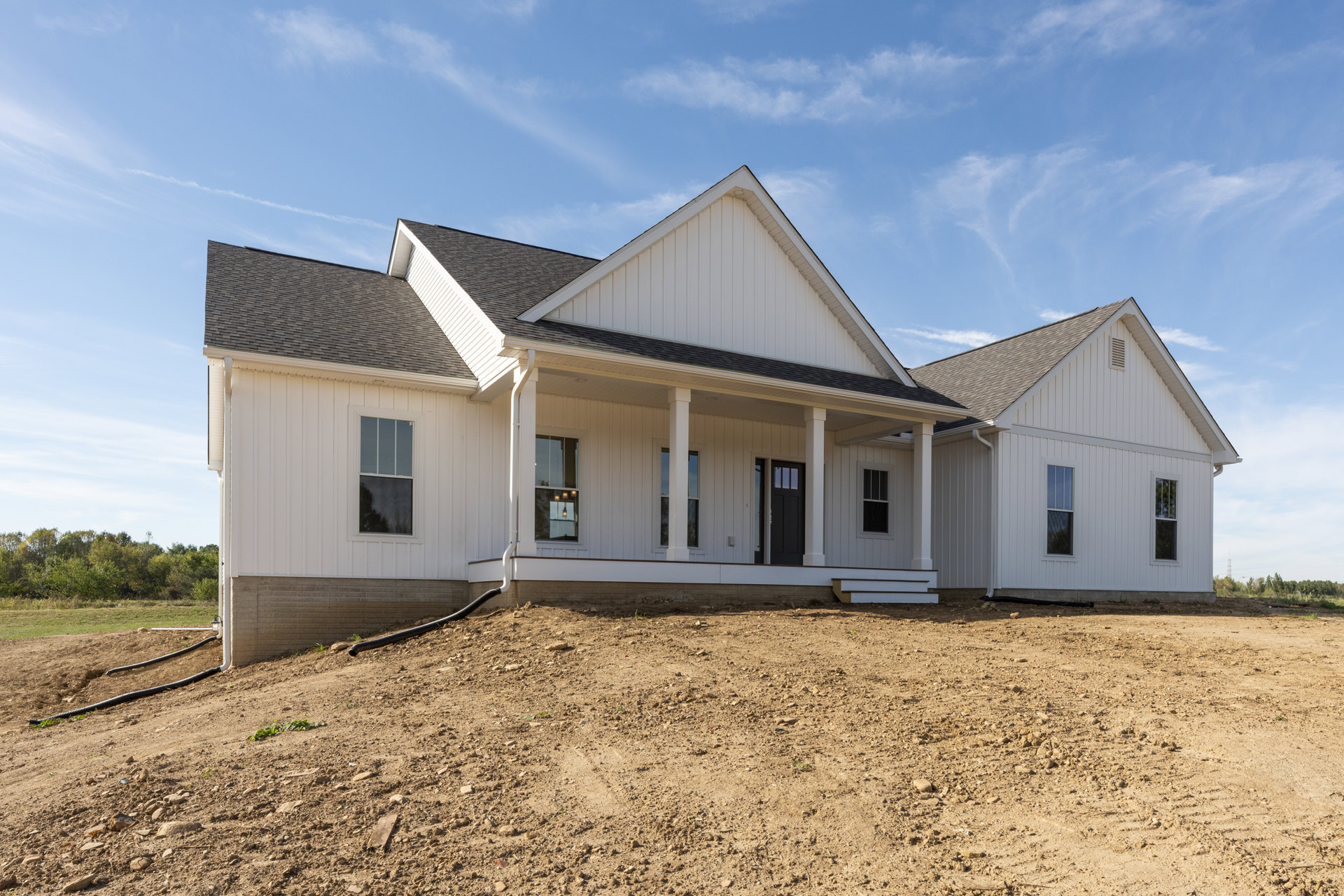 White house with white siding and porch, set against a dirt hill and open field, white-framed windows, scattered trees in background, partly cloudy sky overhead