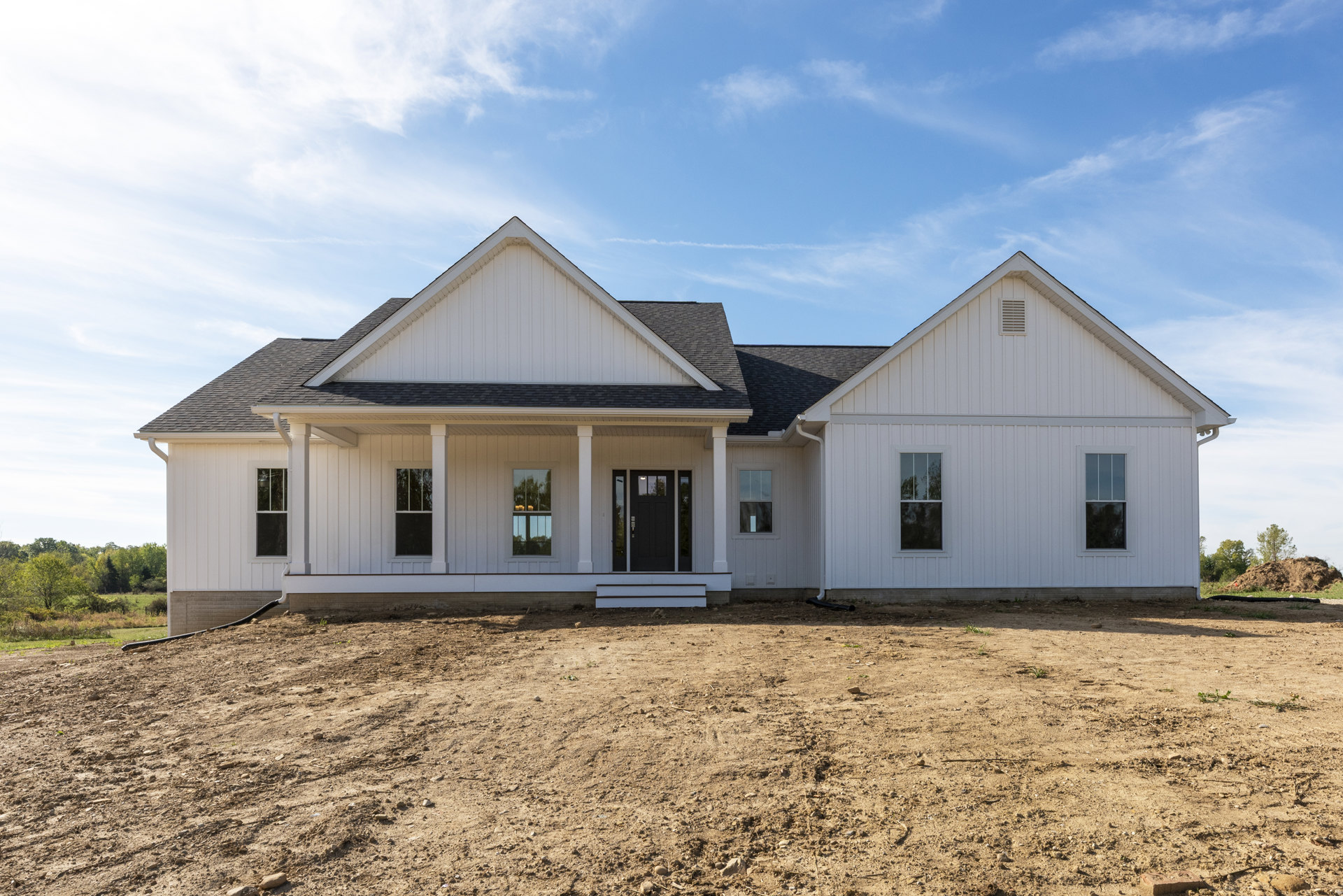 White house with black door and glass panel, white-framed window displaying candles, set beside a dirt field under a cloudy sky