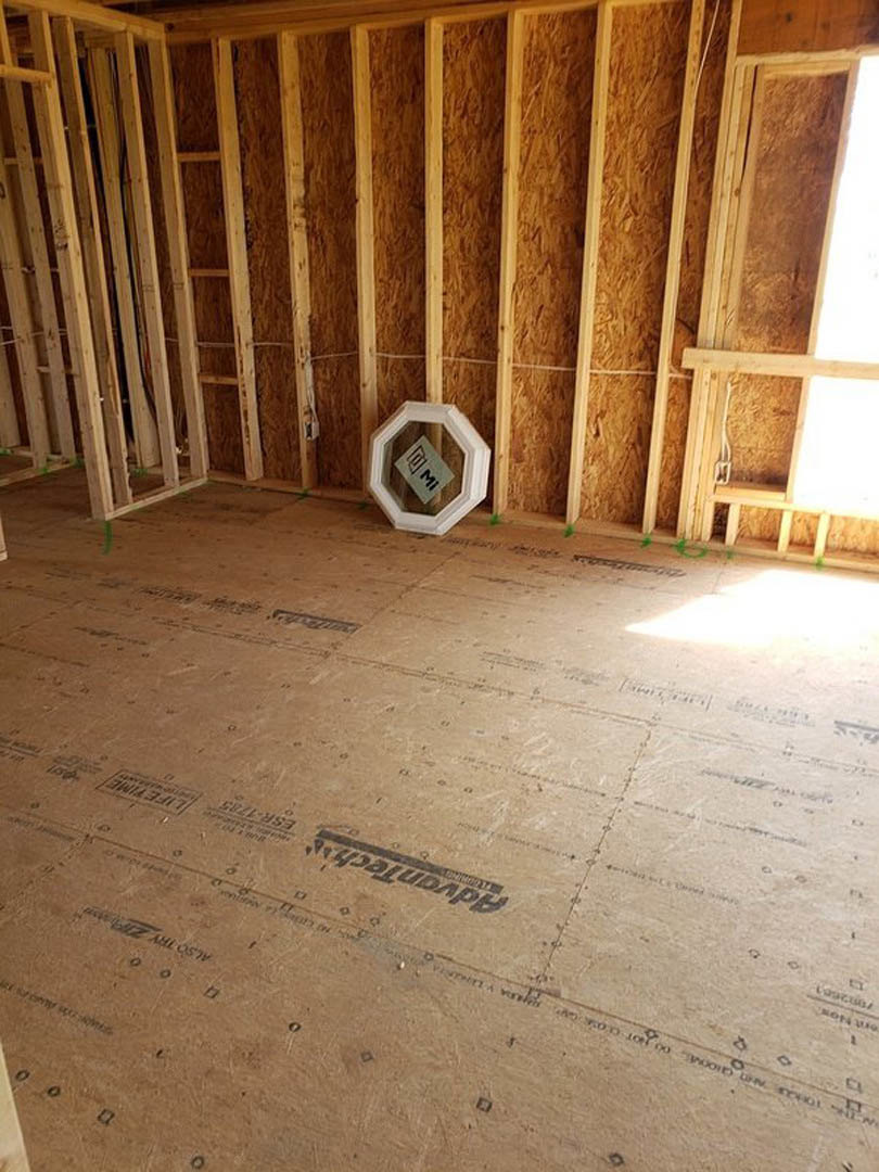 Wood-framed room with exposed beams, unfinished wood floor, white sign with black lettering leaning against wall