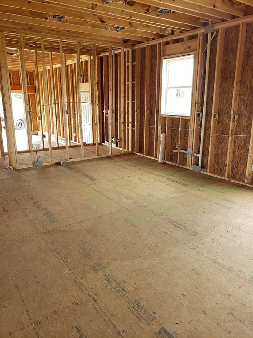 Wood-framed room under construction with exposed beams, unfinished walls, and a white-framed window letting in natural light