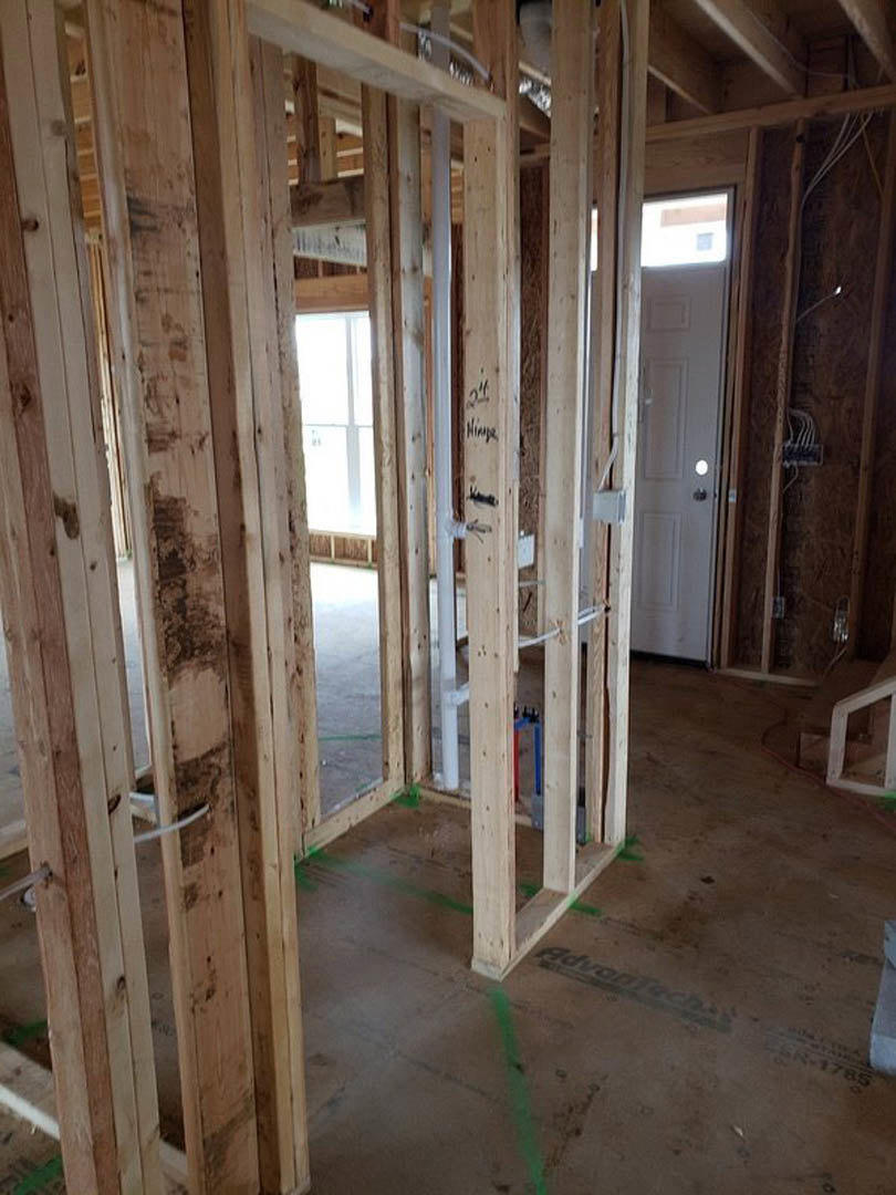 Room under construction with exposed wood framing, partially installed door, white metal bar with brown surface, window allowing natural light, and visible building insulation