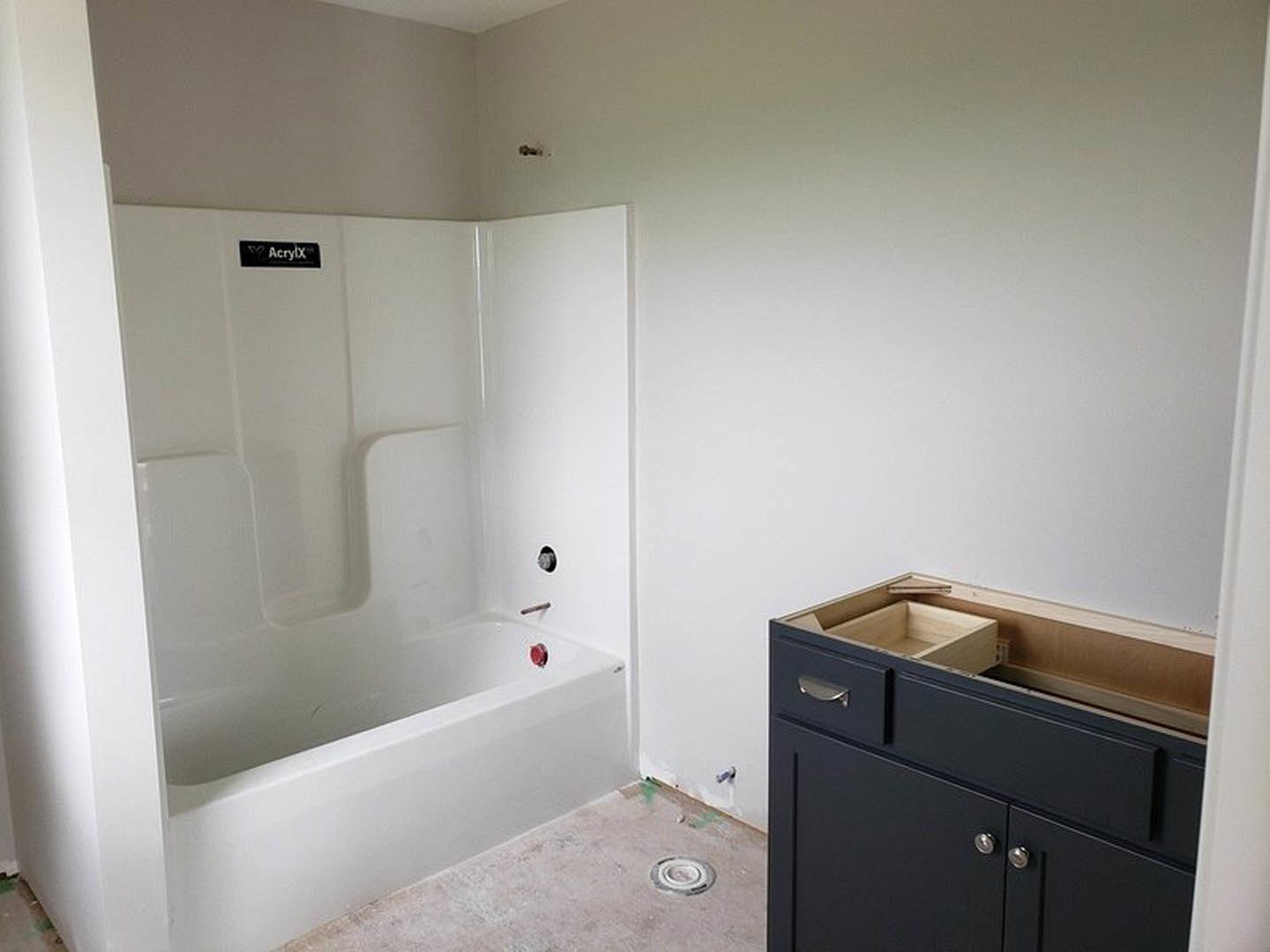 White freestanding bathtub beside a modern vanity with open wooden drawers, light tile flooring, and sleek chrome fixtures