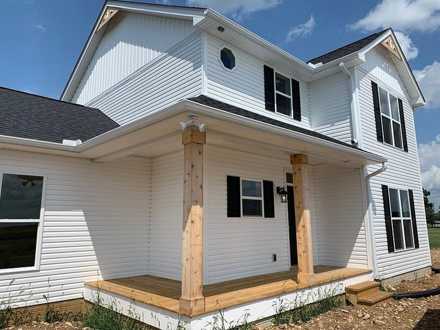 White siding house with covered porch, wood support beams, white-framed windows, and black hexagonal accent on exterior wall