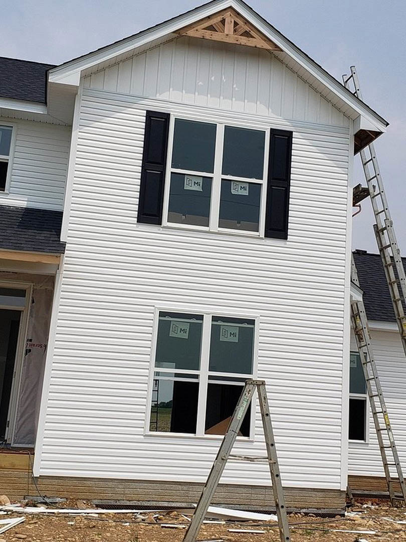 White siding exterior with black shuttered windows, white trim, and a ladder leaning against the wall near a white door with red text