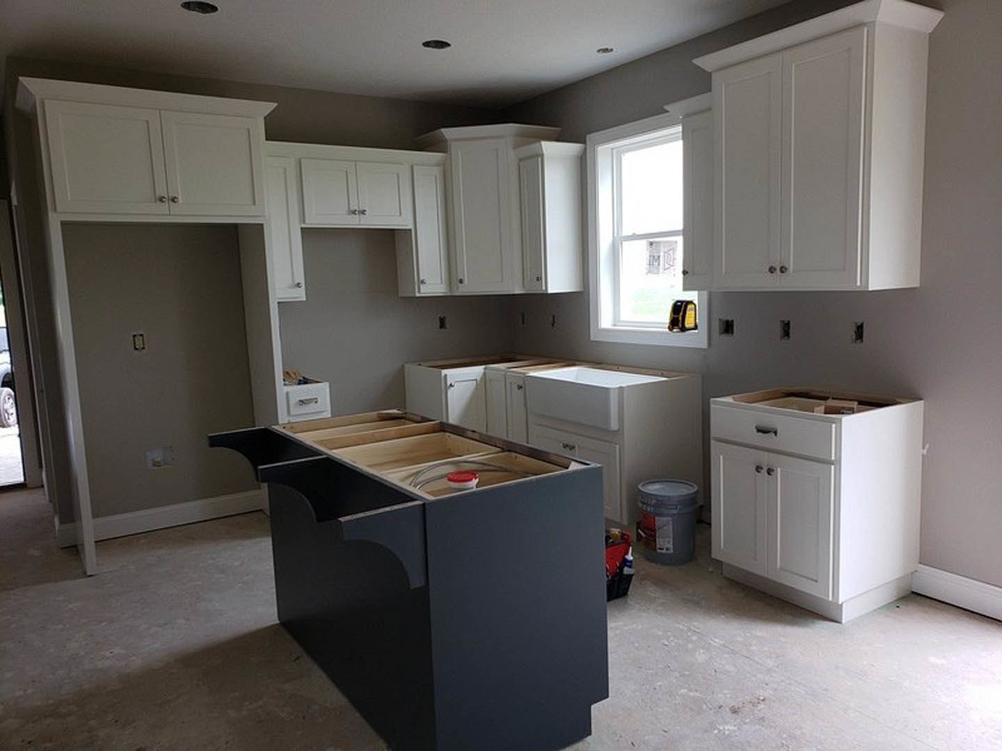 White kitchen cabinets with silver hardware, black island featuring drawers, stainless steel appliances, light stone countertops, wood flooring, window with paper taped to glass