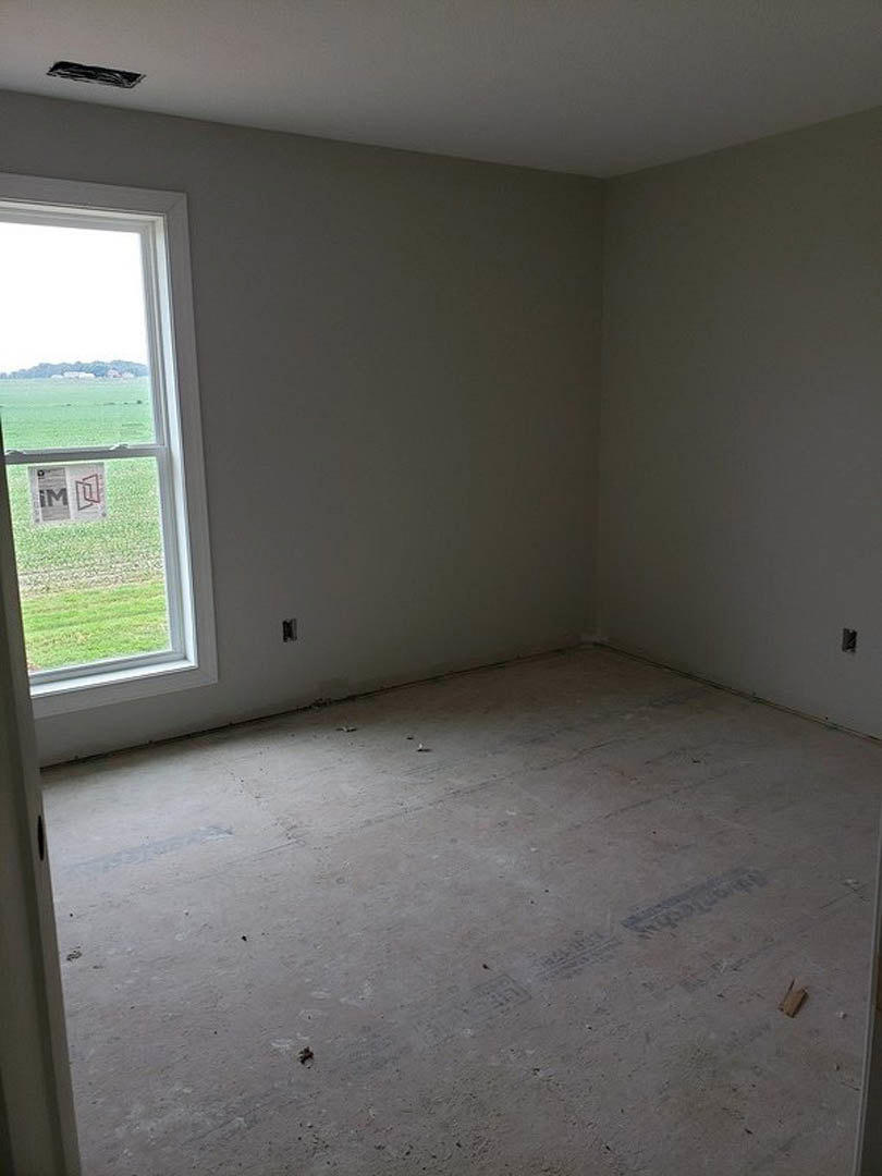 Sunlit room with white plaster walls, large window overlooking green field, light flooring, and minimal furnishings